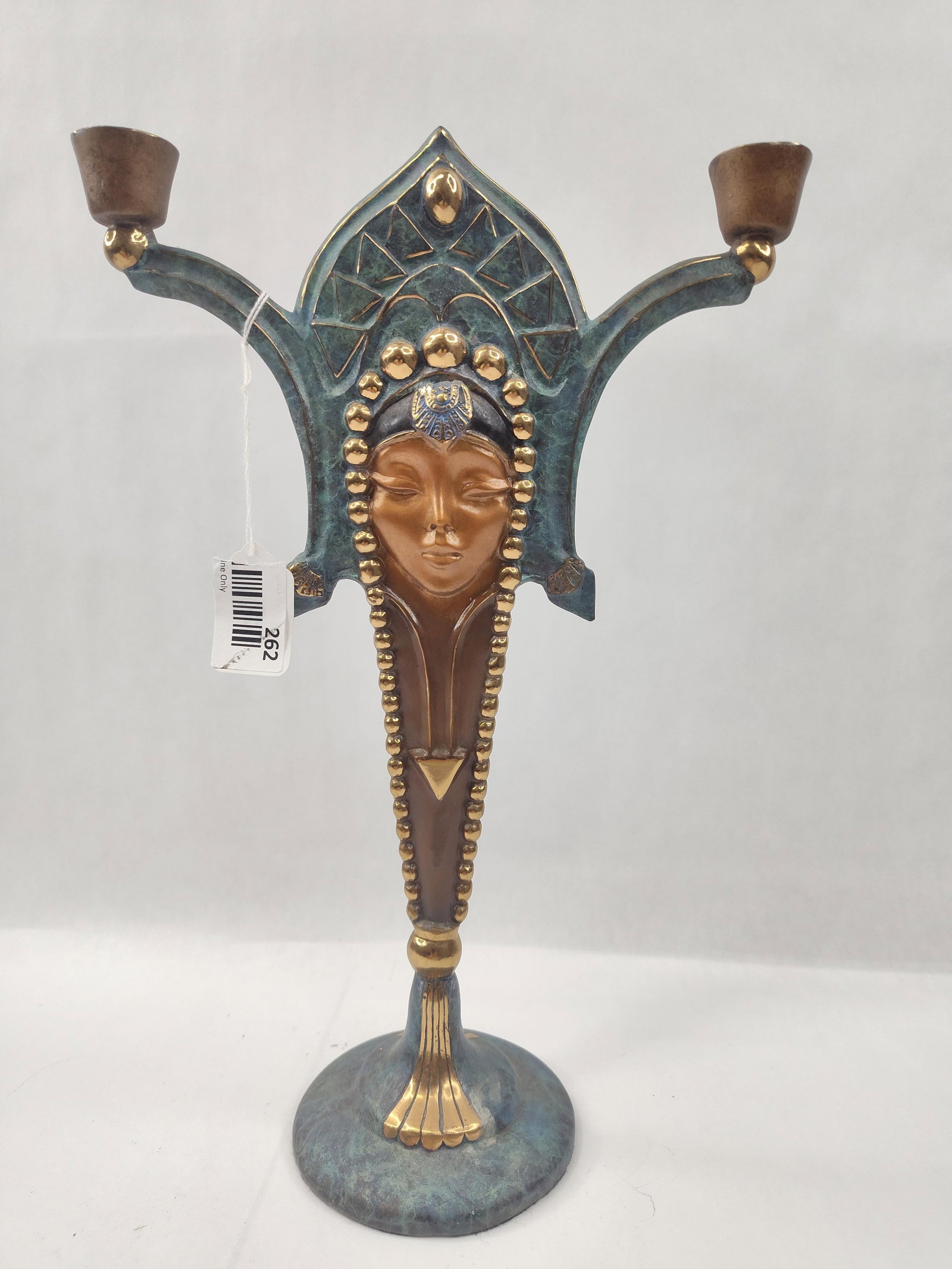 Art Deco Polychrome Bronze Candelabra: This two-light candelabra is constructed in an Art Deco style, featuring a central stylized female face set within an elaborate headdress. The piece is finished with a polychrome patina, displaying a 