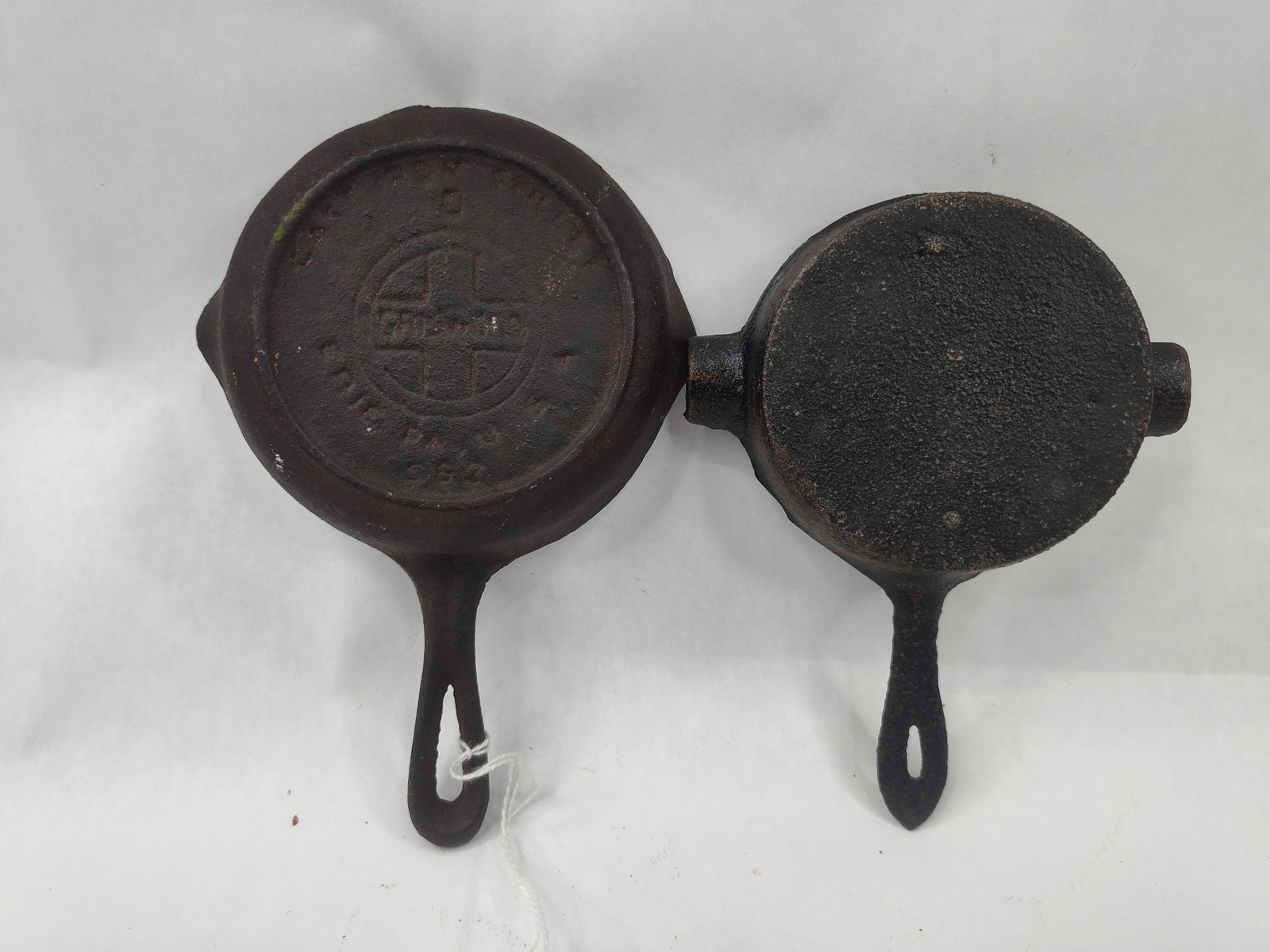 Griswold & Ashley Cast Iron Pair: This lot comprises two cast iron items. The first is a small cast iron skillet featuring a heat ring on the underside. The base bears an impressed circular mark. In the center is a cross inside a