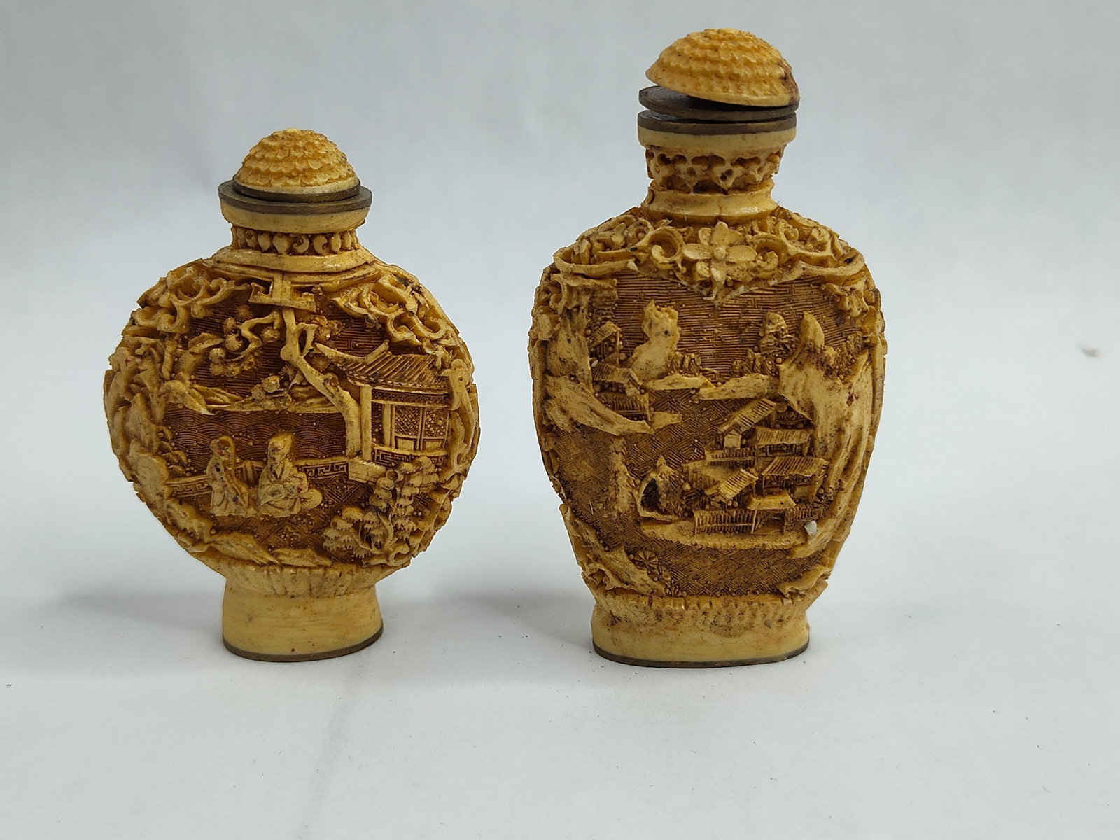 Pair Landscape Carved Resin Snuff Btls: A pair of Chinese-style snuff bottles crafted from a yellowed resin material, designed to simulate carved cinnabar lacquer or ivory. One bottle features a compressed globular form, while the taller co