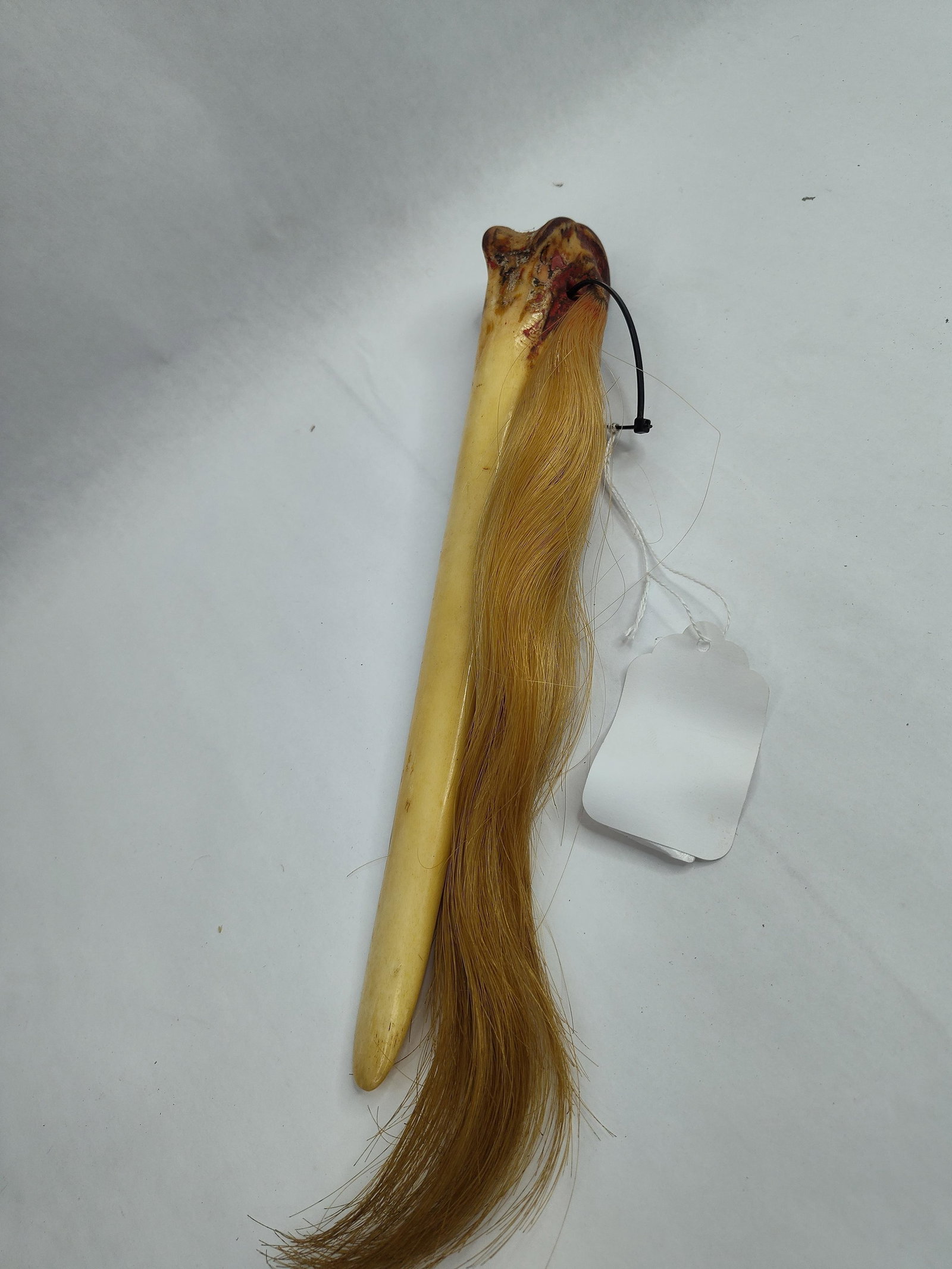 Carved Bone Fly Whisk w/ Horsehair: A ritual or utilitarian implement fashioned from a hollowed animal bone, likely a metapodial or long bone, featuring a horsehair tassel. The bone has been carved into a tapered, scoop-like form with