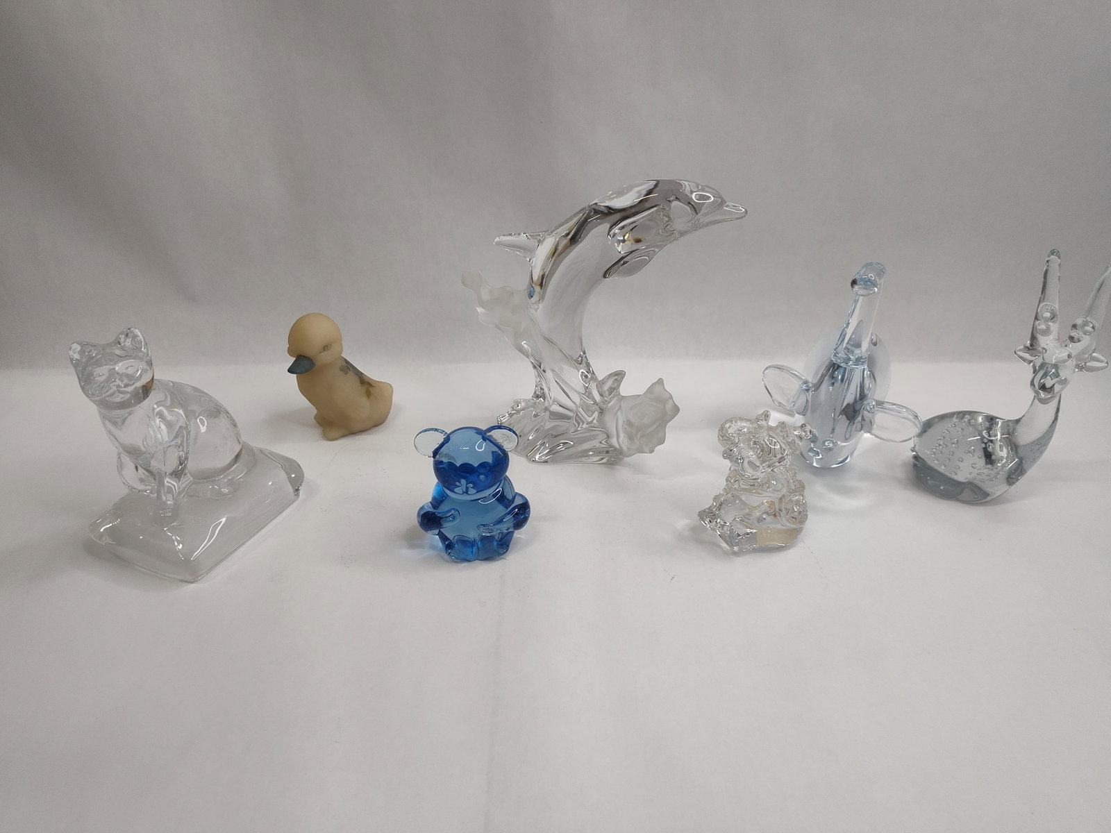 Set Glass Animal Figurines: An assortment of glass animal figurines in various styles and finishes. The collection includes a clear glass dolphin modeled in a leaping position from a frosted, wave-like base; a clear glass