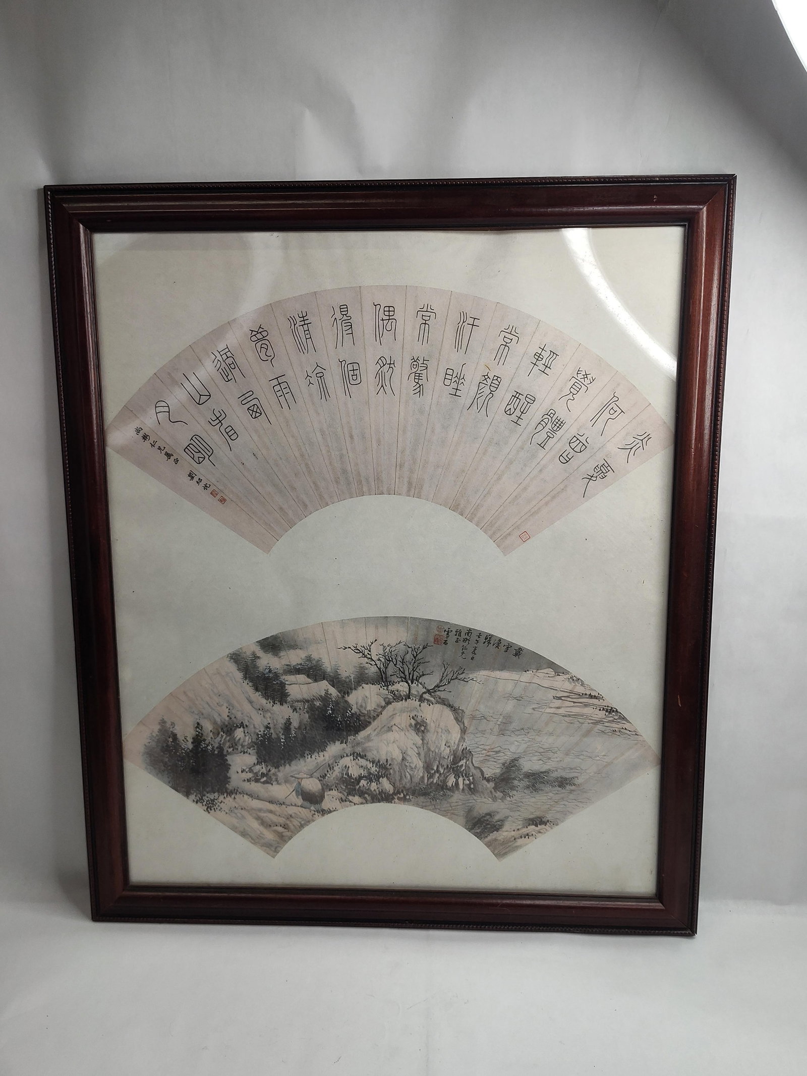 Pair Chinese Ink & Color Paper Fan: A pair of Chinese paper fan leaves, one featuring calligraphy and the other a landscape painting, mounted together and presented in a dark wood frame with a beaded inner edge. The upper fan leaf