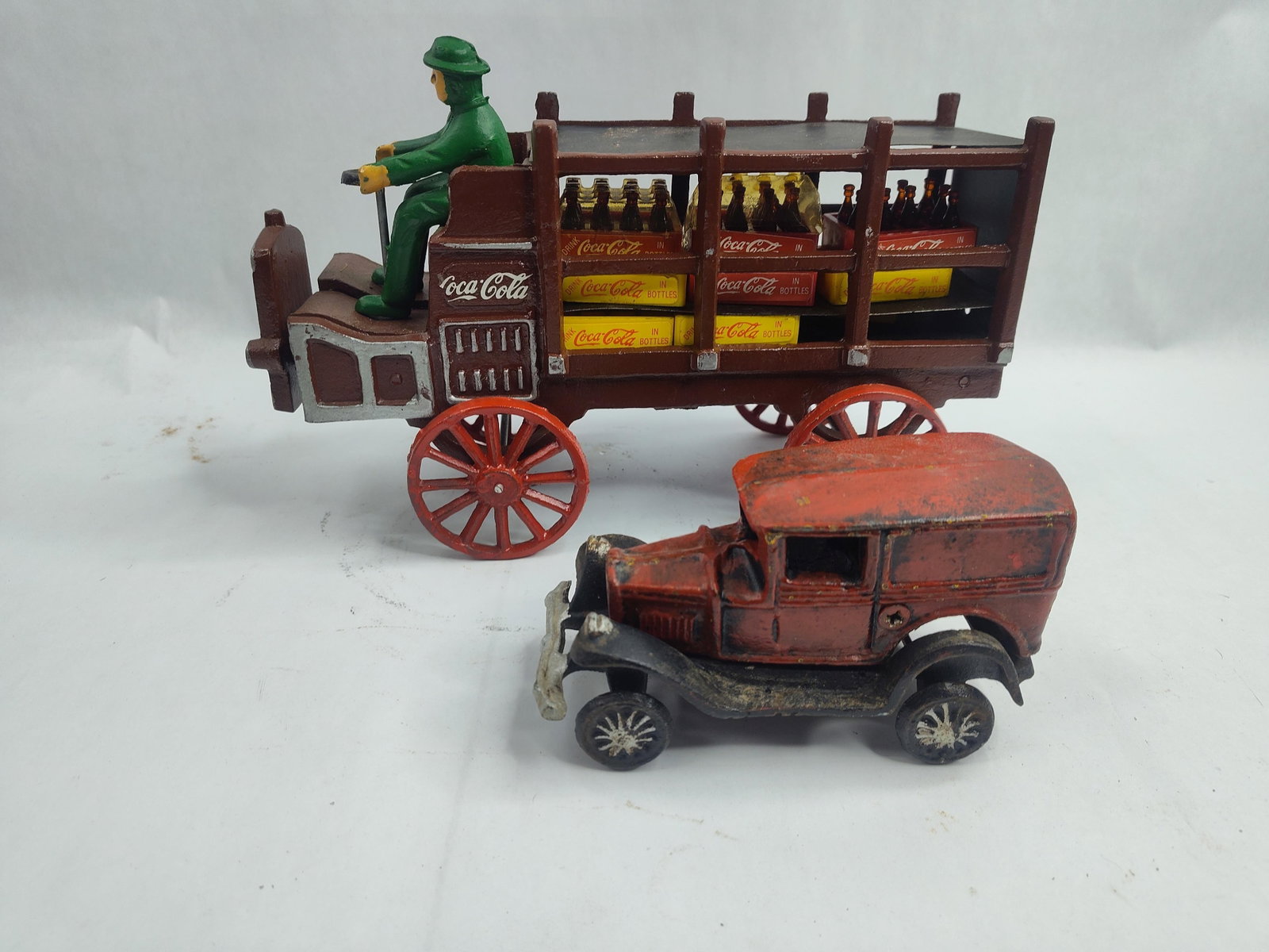 2 Cast Iron Coca-Cola & Red Model Vans: A collection of two -style cast iron vehicles comprising a Coca-Cola delivery truck and a red panel van. The delivery truck is constructed of heavy cast iron with a brown painted body and red spoke