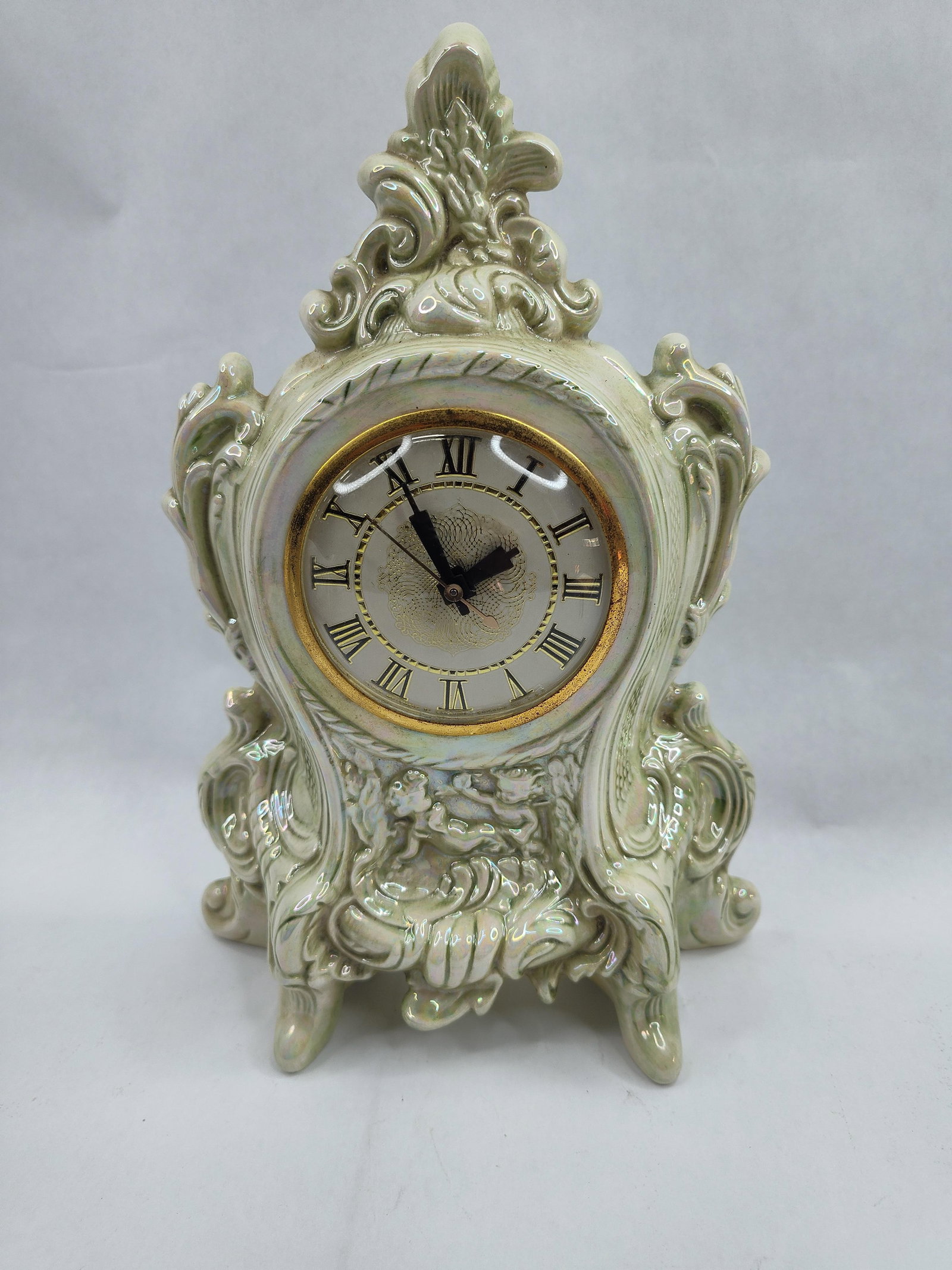 Lanshire Ceramic Mantel Clock, 1969: A Lanshire electric mantel clock featuring a molded ceramic body with an iridescent lusterware glaze and rococo-style scrolling flourishes throughout the form. The front of the case is decorated in