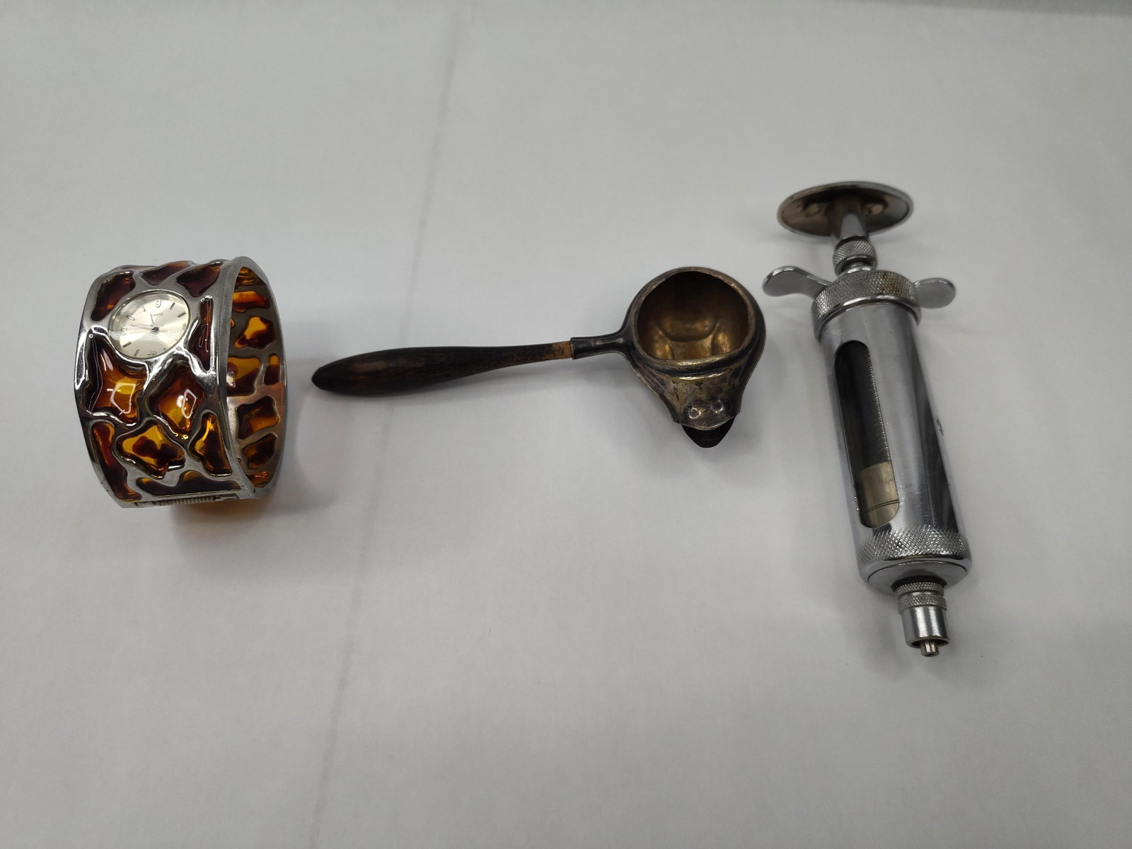 Vaco Syringe, Silver Spoon & Watch Lot: This lot comprises three distinct objects: a large-format medical instrument, an feeding spoon, and a modern fashion timepiece. The first item is a chrome-plated metal and glass syringe. The body
