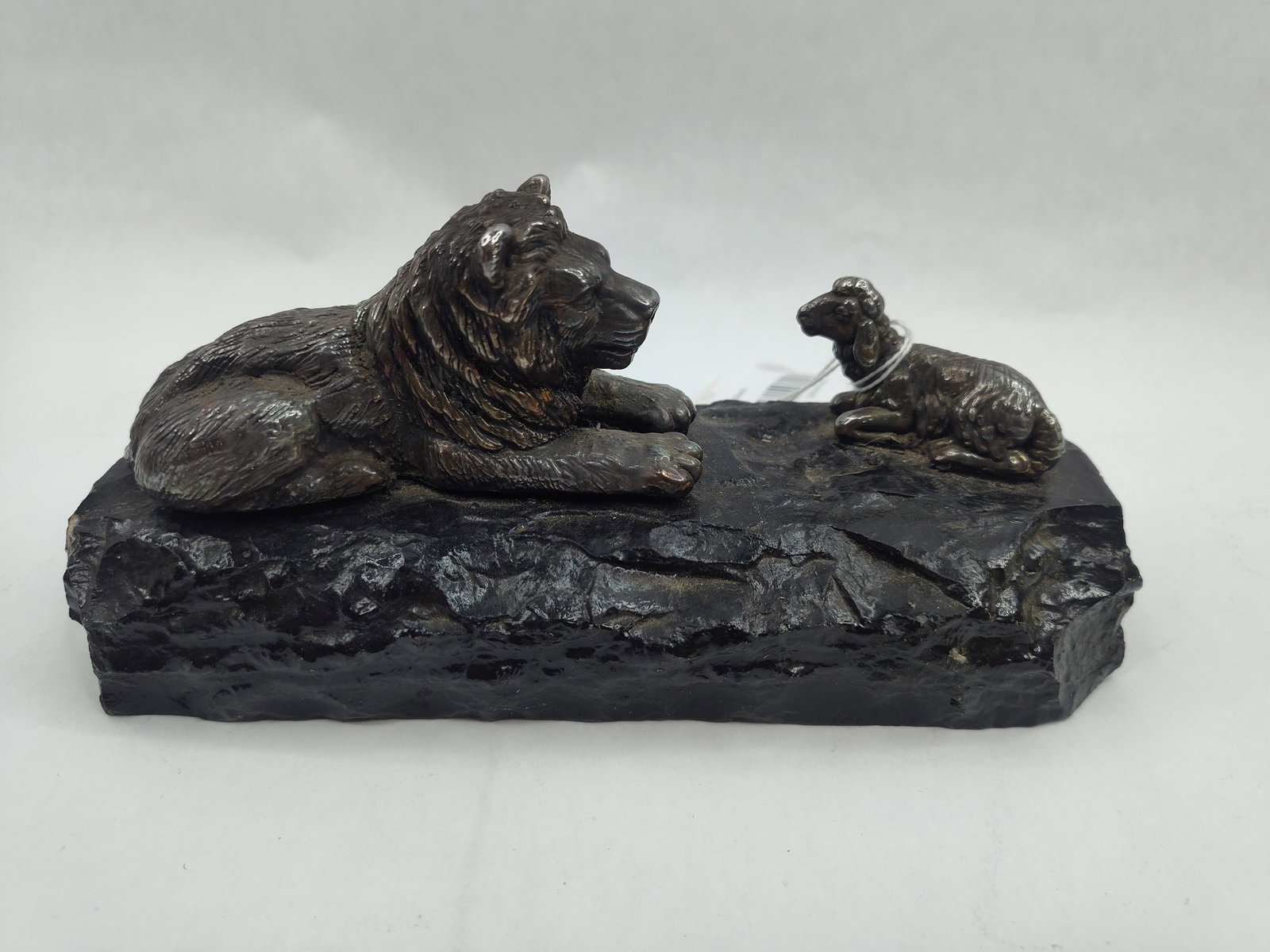 Lion & Lamb Metal Sculpture on Stone: A decorative metal sculpture in the animalier style, depicting a lion and a lamb in a reclining pose, facing one another. The two figures are cast with a dark, textured surface showing