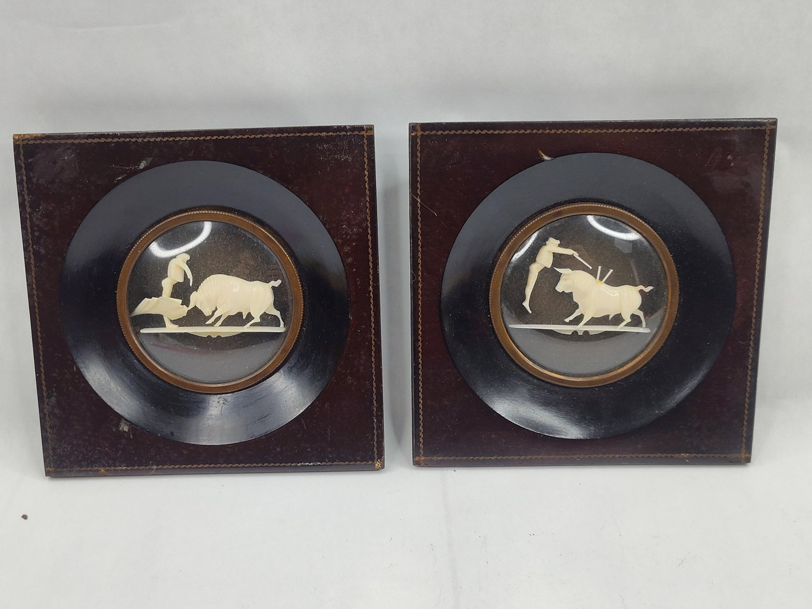 Pair Spanish Carved Ivory Bull Dioramas: A pair of Spanish hand-carved ivory dioramas depicting traditional bullfighting scenes. Each diorama features a high-relief ivory carving mounted within a circular deep-well frame. The first diorama
