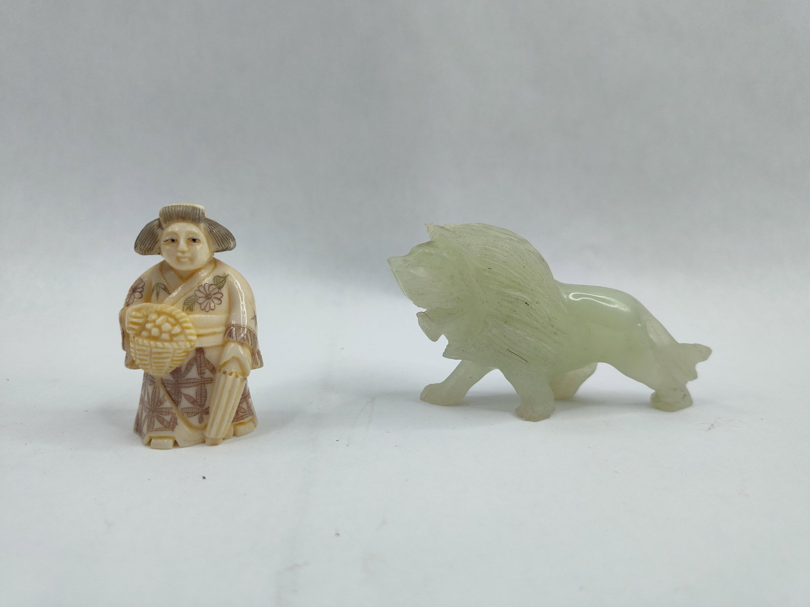 Pair Asian Figures: Netsuke & Stone: This lot comprises two small carved sculptures. The first is a Japanese netsuke-style figure of a woman, possibly a geisha or fruit seller, standing in a decorated kimono. She is depicted holding a wo