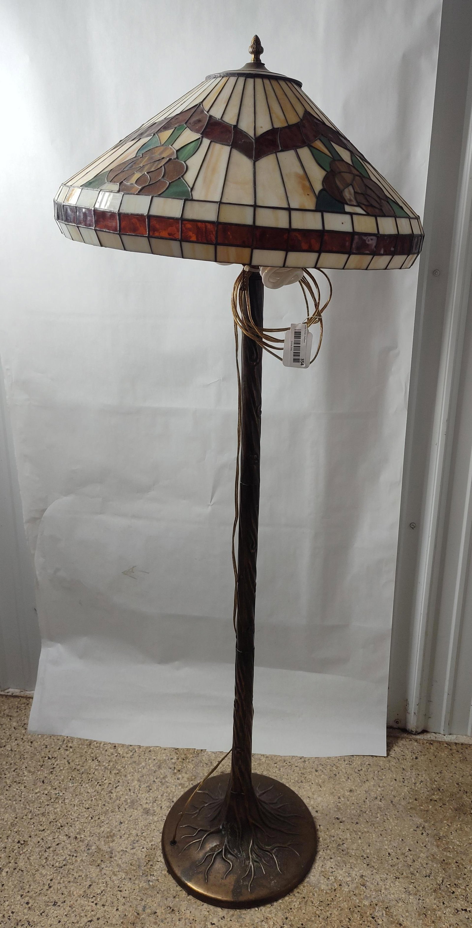 Tiffany Style Leaded Glass Floor Lamp: This floor lamp consists of a leaded glass shade and a cast metal base. The shade is constructed in a Tiffany style with a geometric background of cream-colored slag glass panes. A central decorative