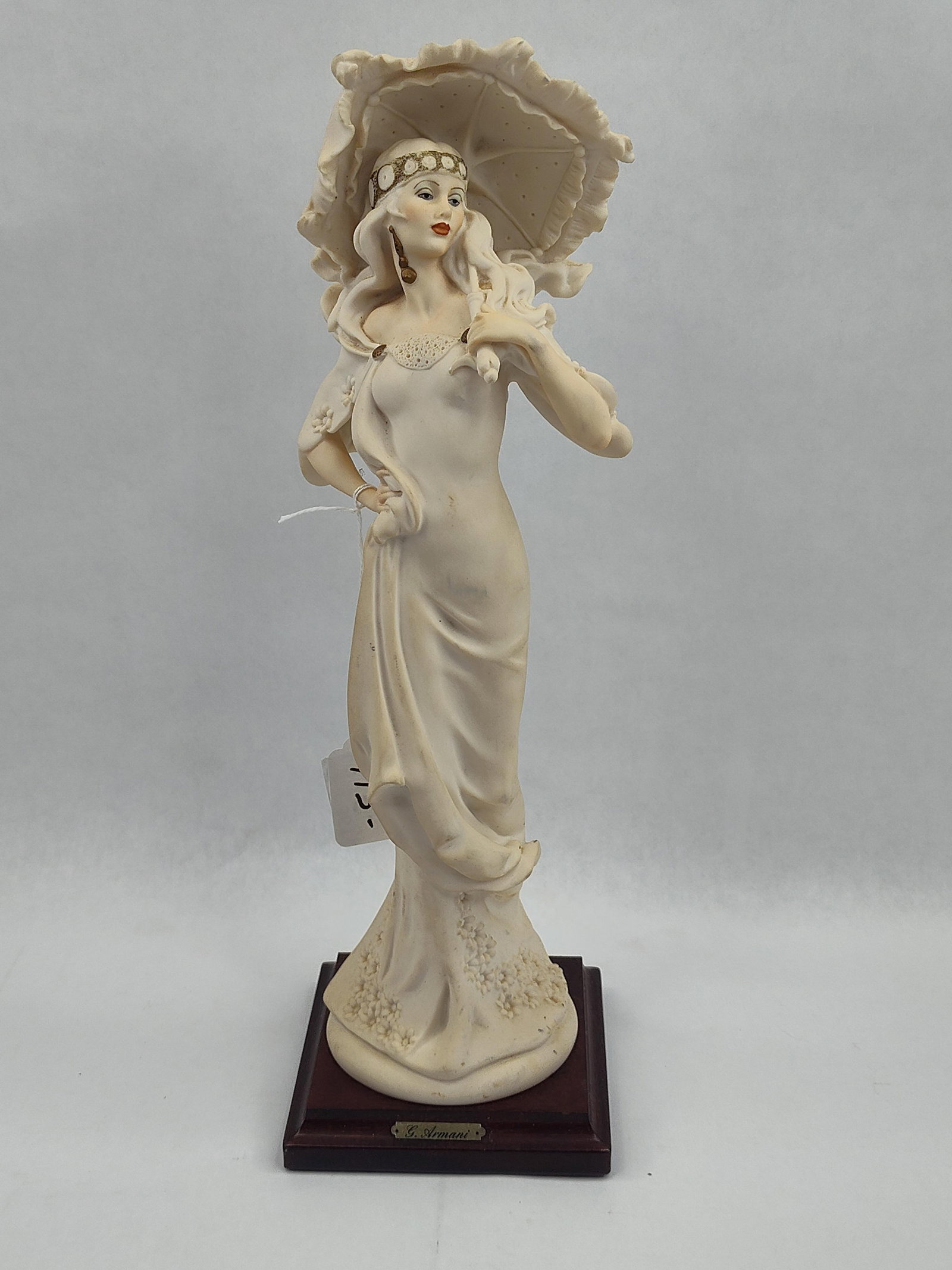 G. Armani Lady w/ Parasol Porc: A Giuseppe Armani cold-cast porcelain figurine depicting a woman in early 20th-century fashion. The figure is rendered in a matte cream finish and stands in a contrapposto pose, holding a ruffled para