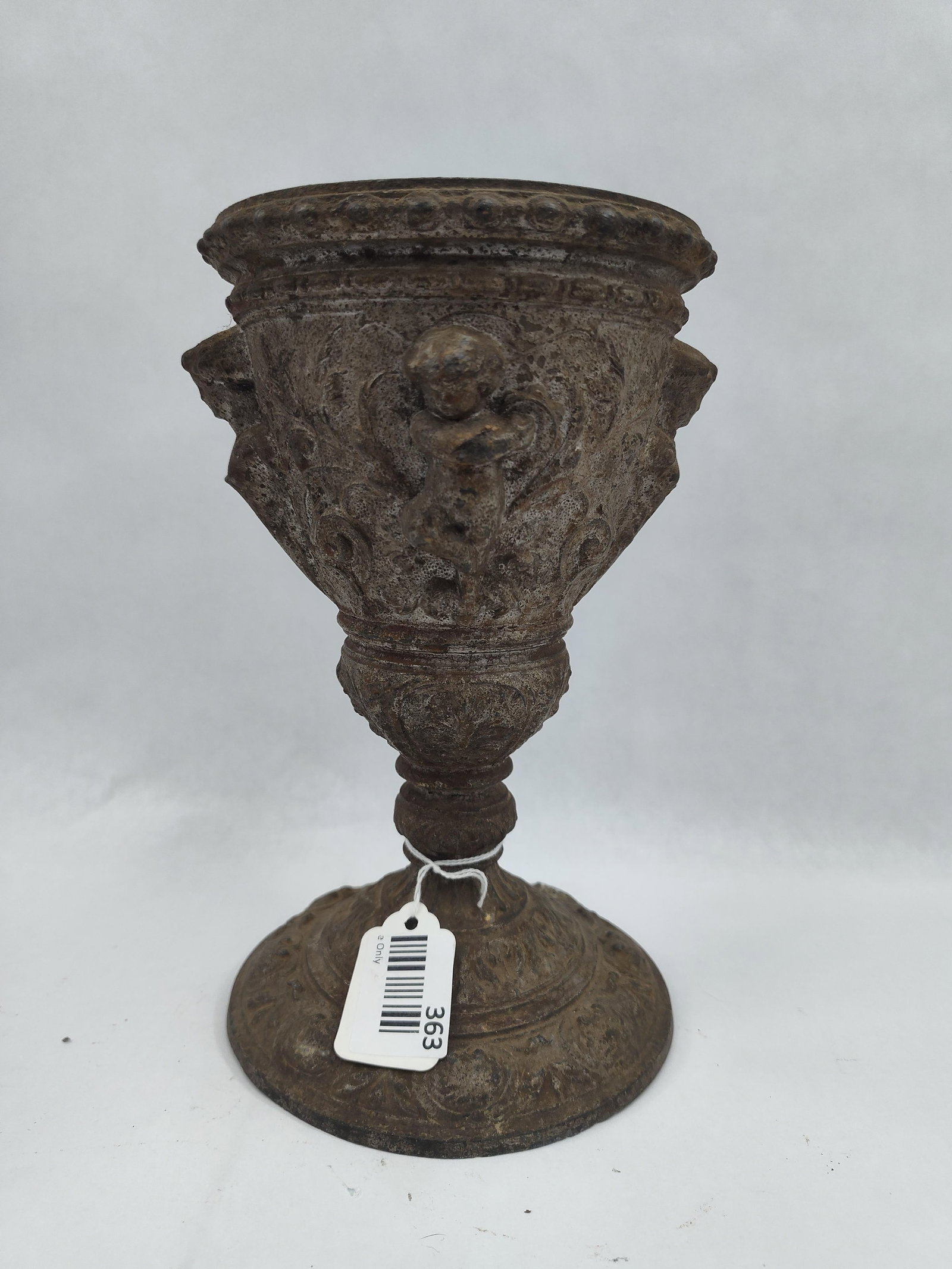 Cast Metal Urn w/ Cherub Reliefs: A cast metal urn or chalice featuring an ornate classical design. The vessel is constructed with a flared rim decorated with a beaded or gadrooned edge, above a tapered body. The exterior of the bowl