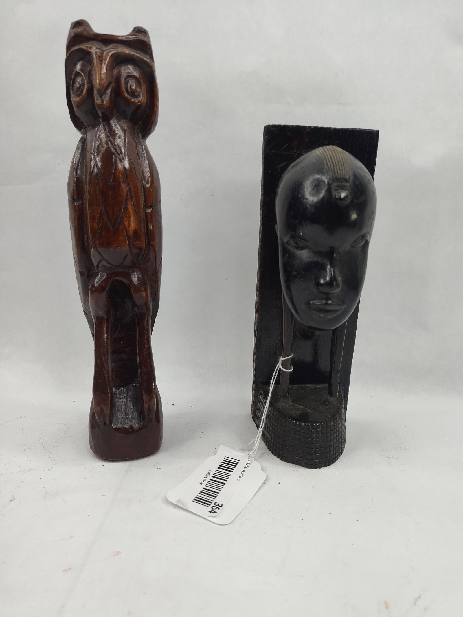 Two Hand Carved Wooden Sculptures: A lot comprising two hand-carved wooden figures. The first is a stylized owl, carved from a reddish-brown wood with a polished finish. The figure features large circular eyes, a prominent beak, and
