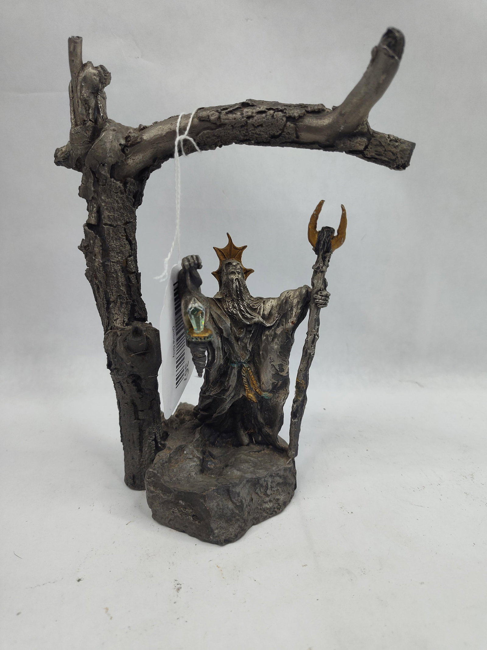 Cast Metal Wizard Figurine w/ Crystal: This cast metal figurine depicts a robed wizard standing upon a rocky outcrop beneath an overhanging gnarled tree branch. The figure is characterized by a long, flowing beard and a crown-like