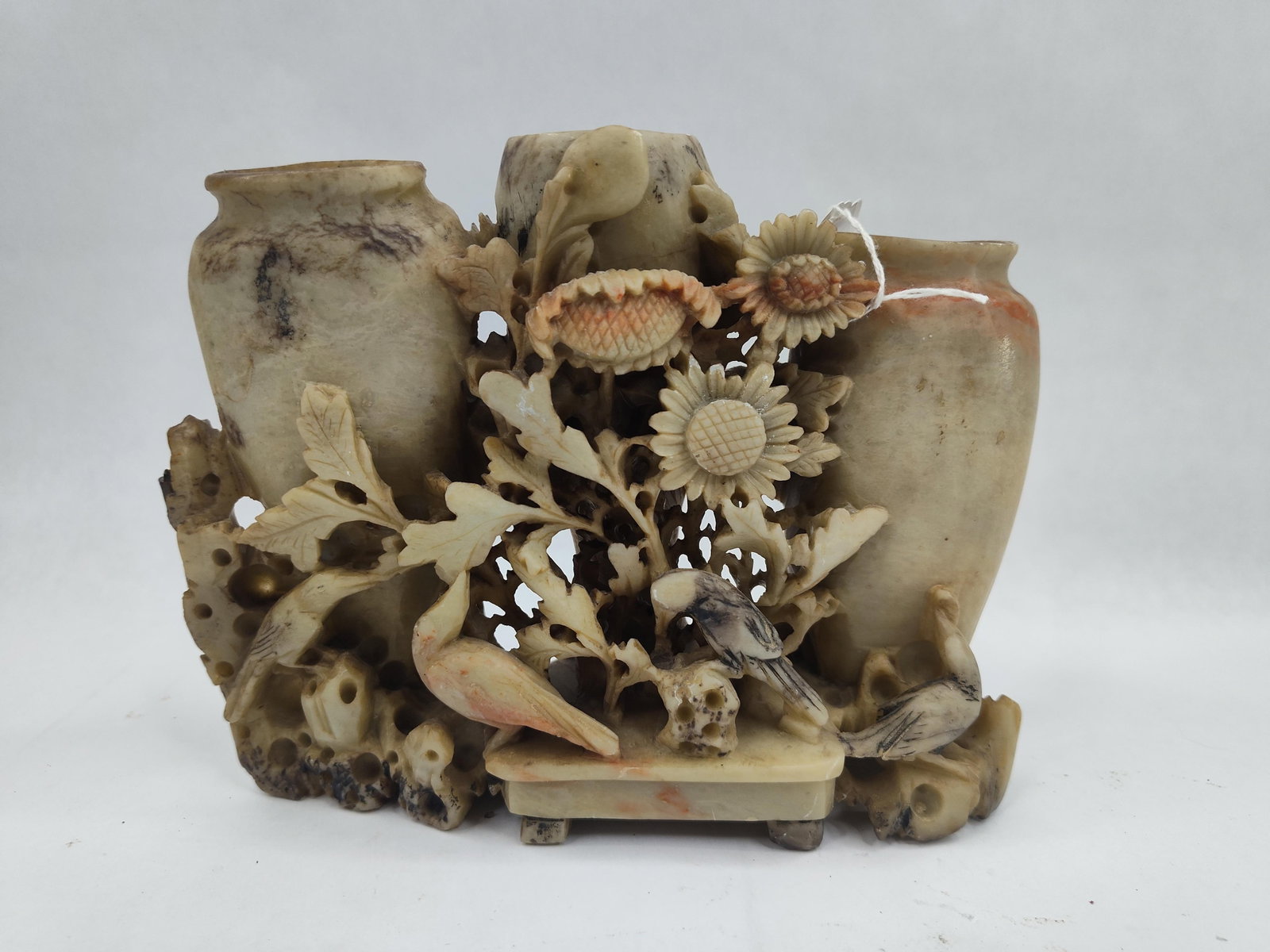 A Carved Soapstone Trio of Vases: A carved soapstone sculptural group featuring three integrated hollowed vessels of varying heights. The central and flanking vases are set within an intricate framework of openwork foliage, including