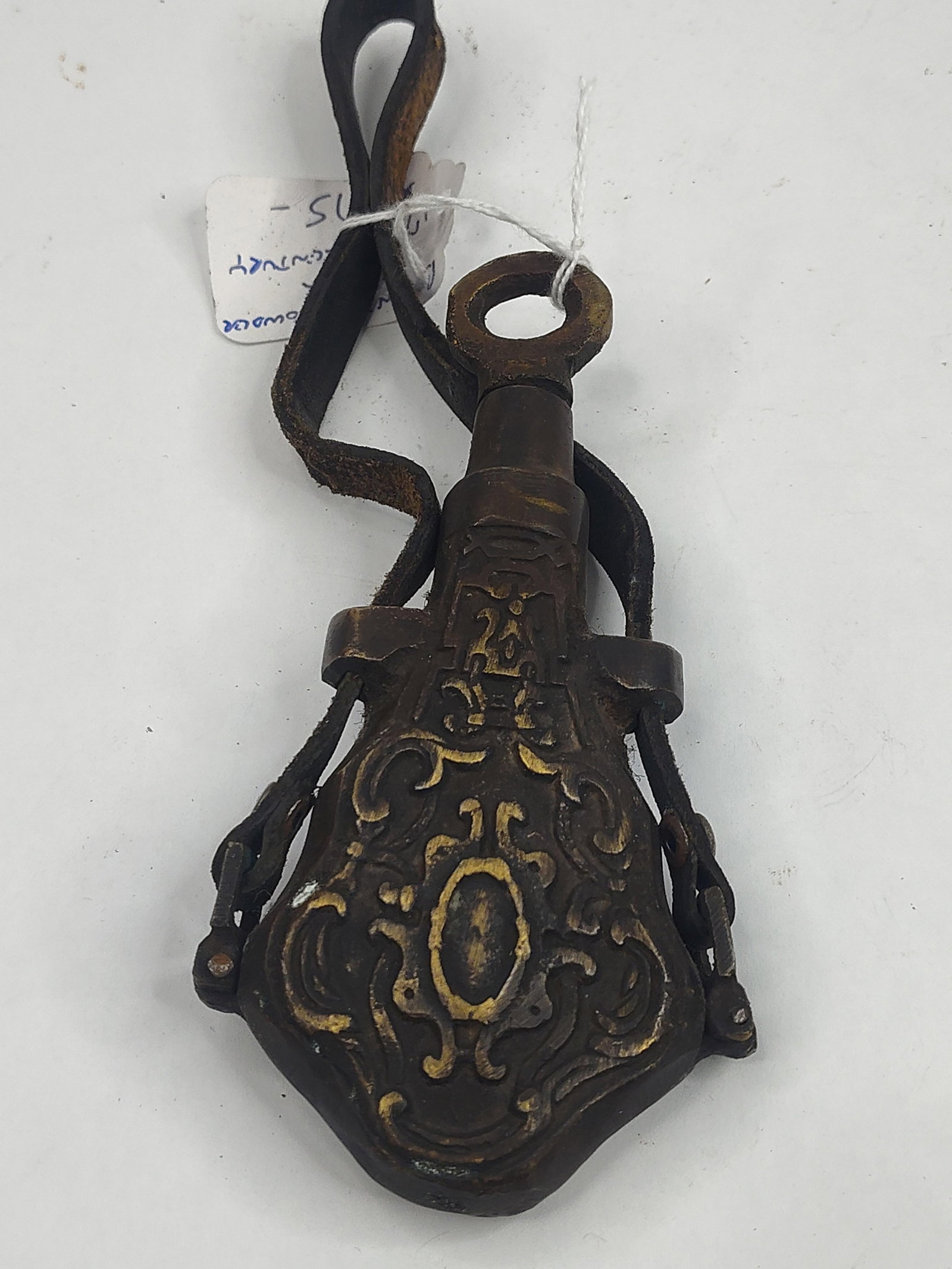Bronze Powder Flask w/ Leather Strap: A decorative cast bronze powder flask featuring rococo-style relief ornamentation. The body is designed with symmetrical scrollwork surrounding a central raised oval medallion on both faces. The