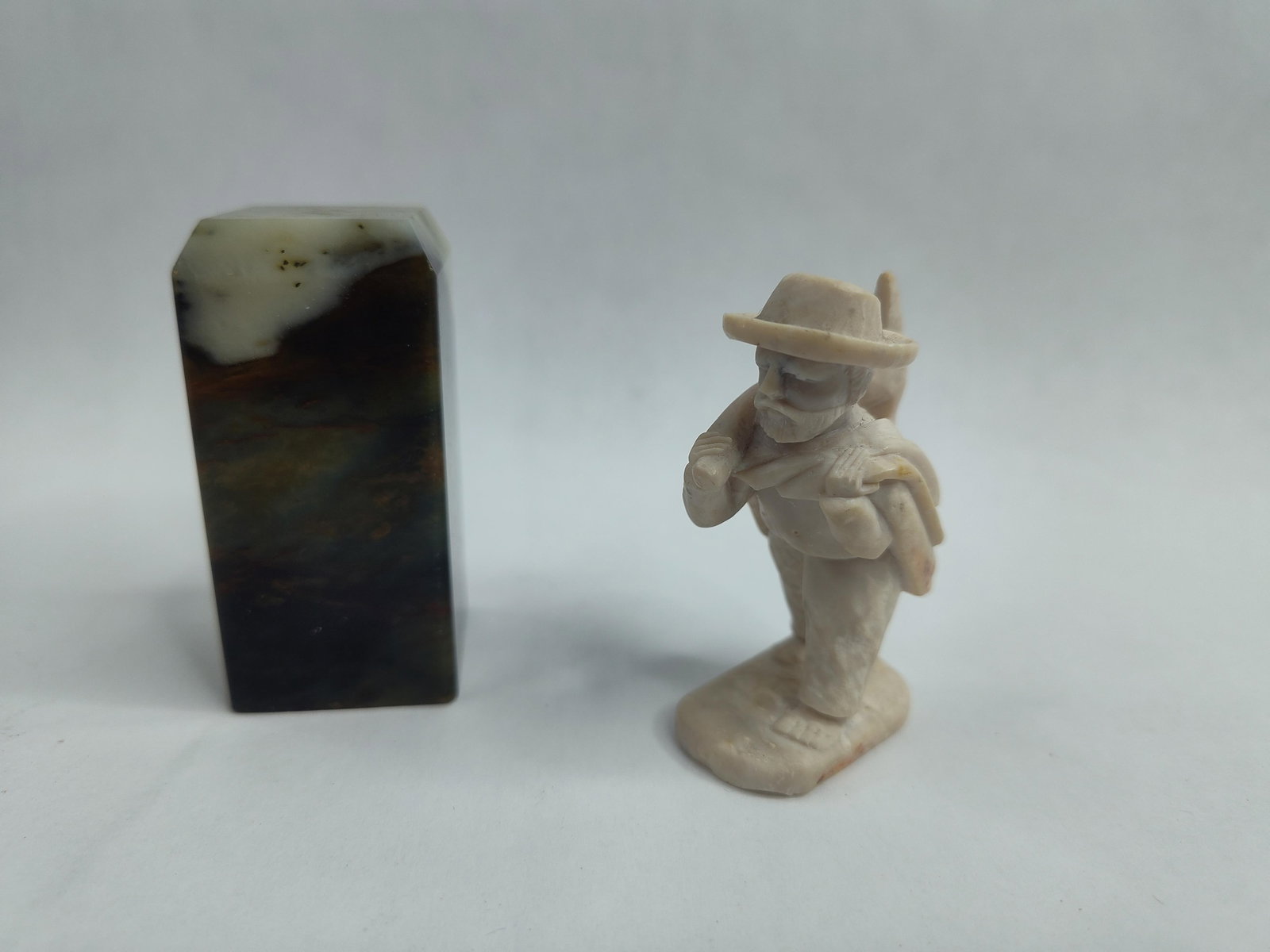 Pair Stone Carvings: Block & Figural: A group of two small stone carvings. The first item is a rectangular lapidary block with chamfered upper edges, fashioned from a multi-colored stone featuring dark green, brown, and ochre banding