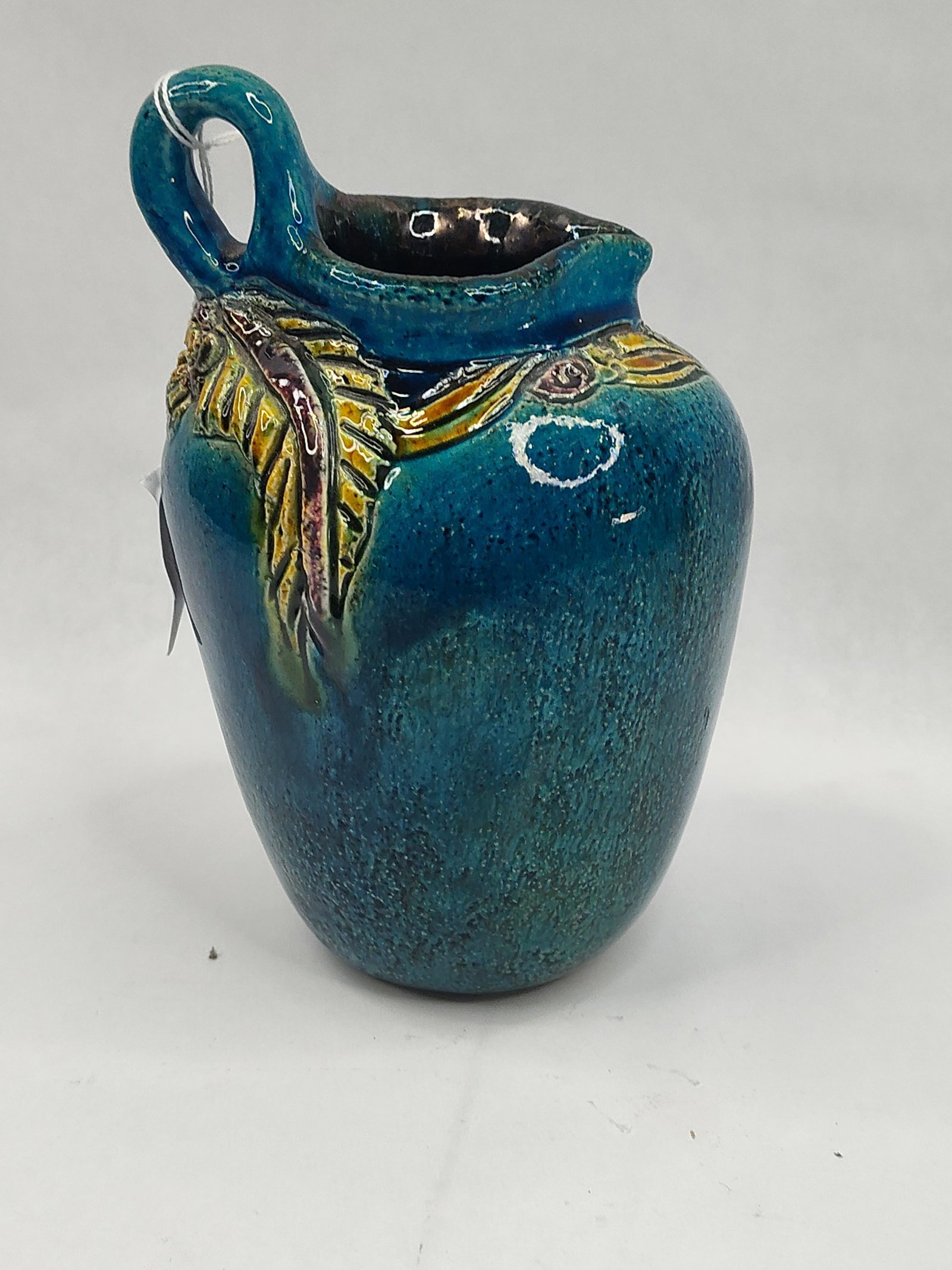 Spanish Glazed Ceramic Pitcher: A small Spanish ceramic pitcher crafted from buff-colored clay. The exterior is finished with a vibrant, mottled turquoise blue glaze featuring a textured, slightly pitted surface. The vessel is