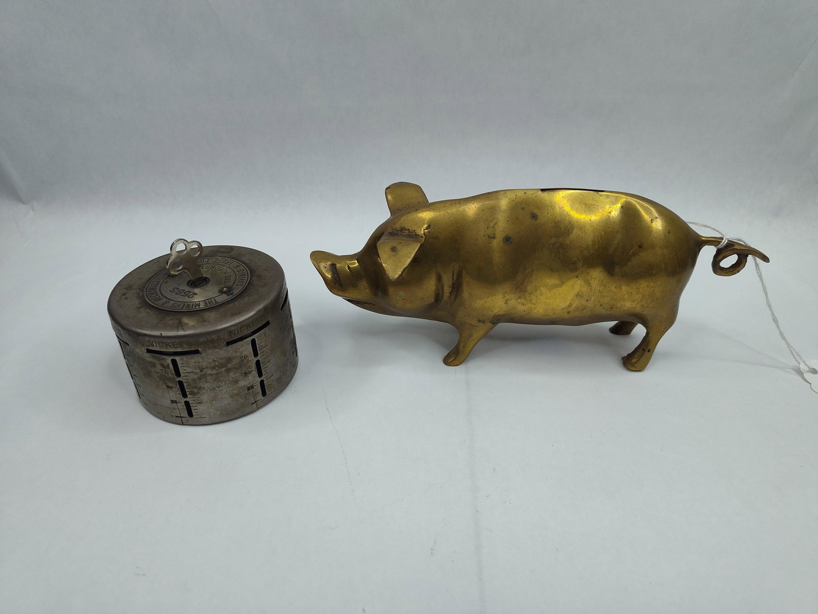 Pair 20th C. Brass & Steel Coin Banks: This group consists of two distinct early 20th-century coin banks. The first is a still bank cast in brass in the form of a stylized pig. The sculpture features a coin slot located on the upper back