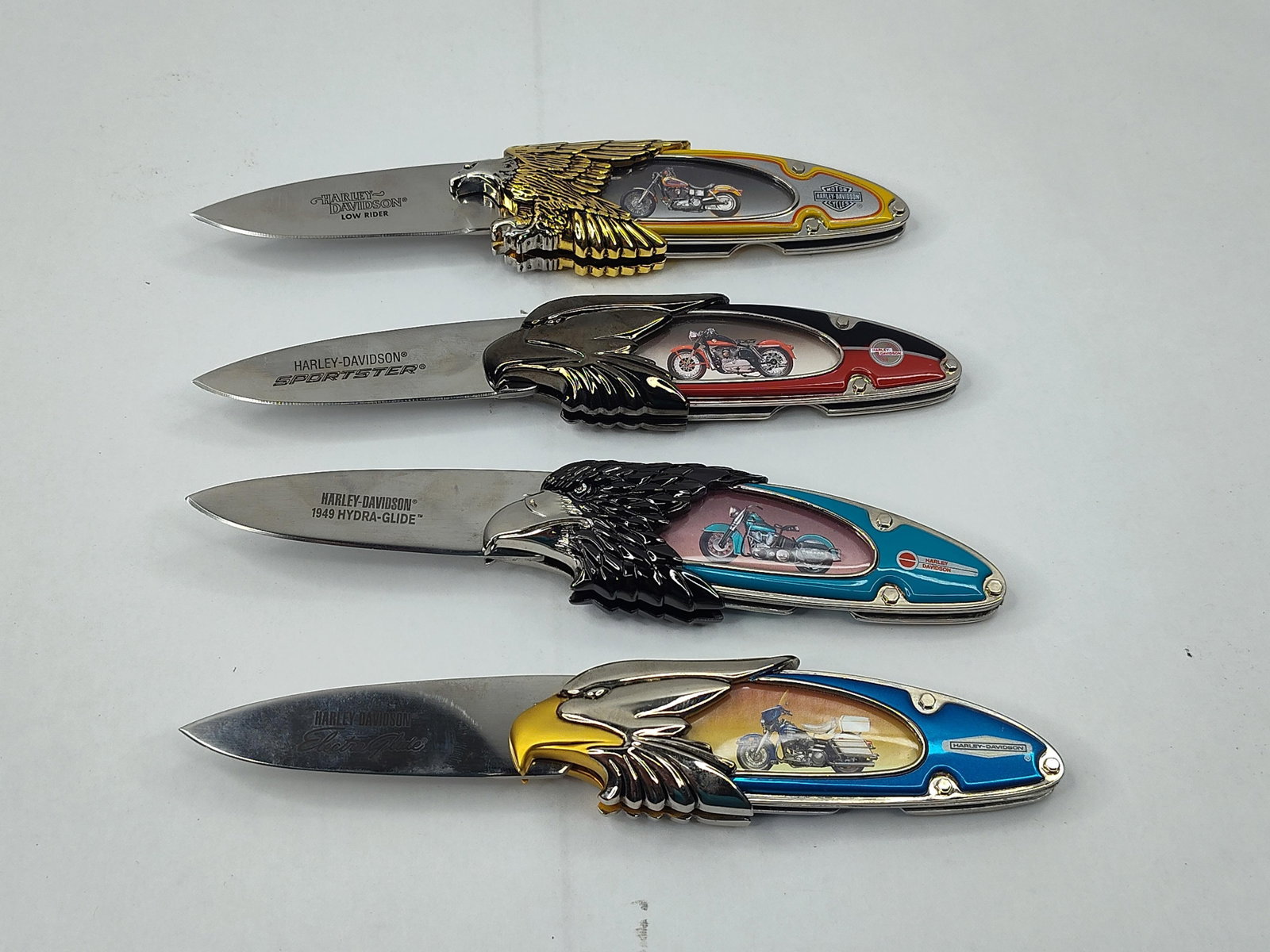 Harley-Davidson Folding Knives Set: This collection features several folding knives, each themed with Harley-Davidson motorcycle motifs. The knives are constructed with decorative bolsters in the form of an eagle head and wings,