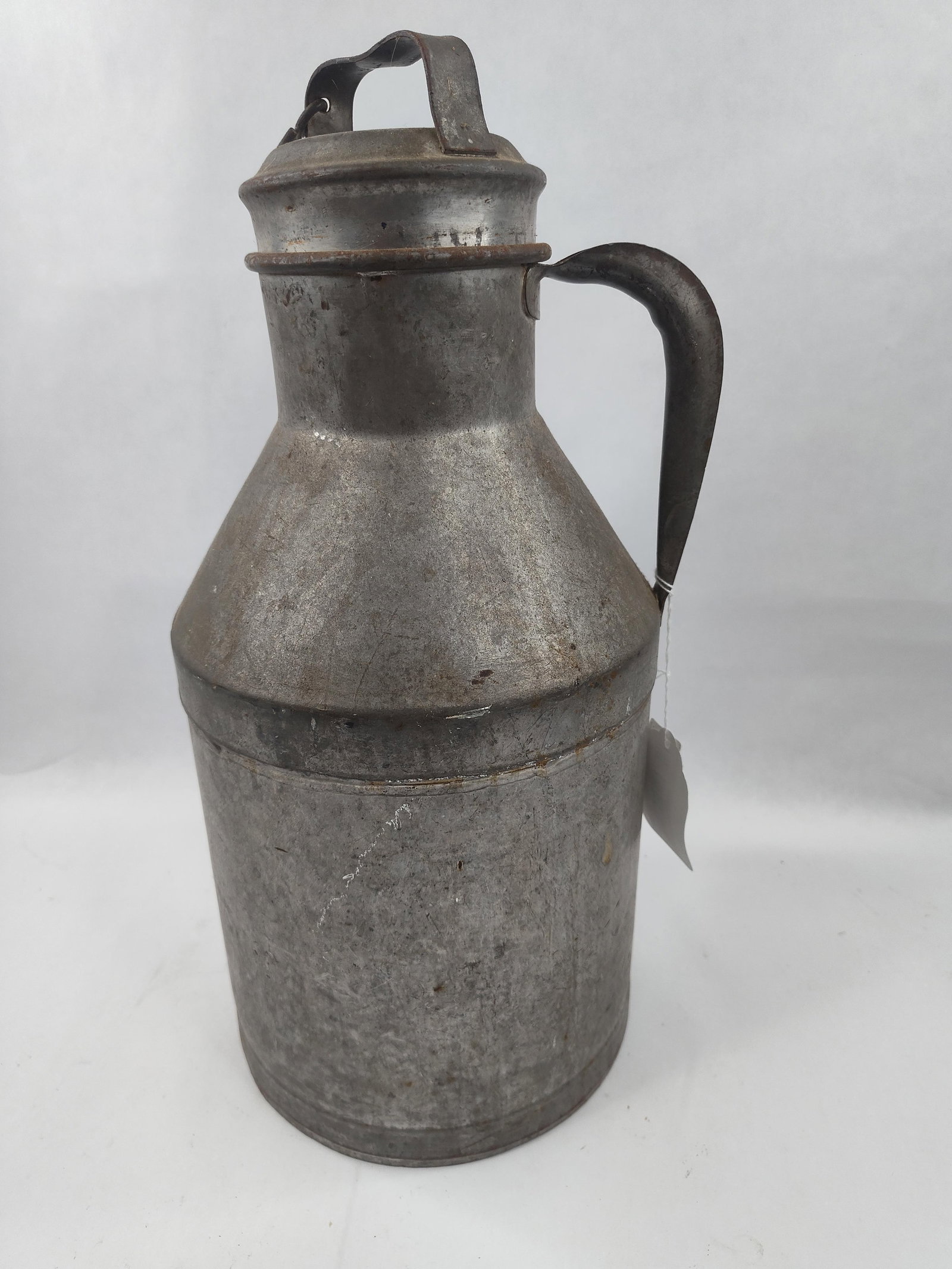 Galv. Metal Milk Can w/ Lid: An dairy vessel constructed from galvanized sheet metal, featuring a cylindrical body that tapers at the shoulder to a narrow neck. The item includes a side-mounted metal handle and a matching top