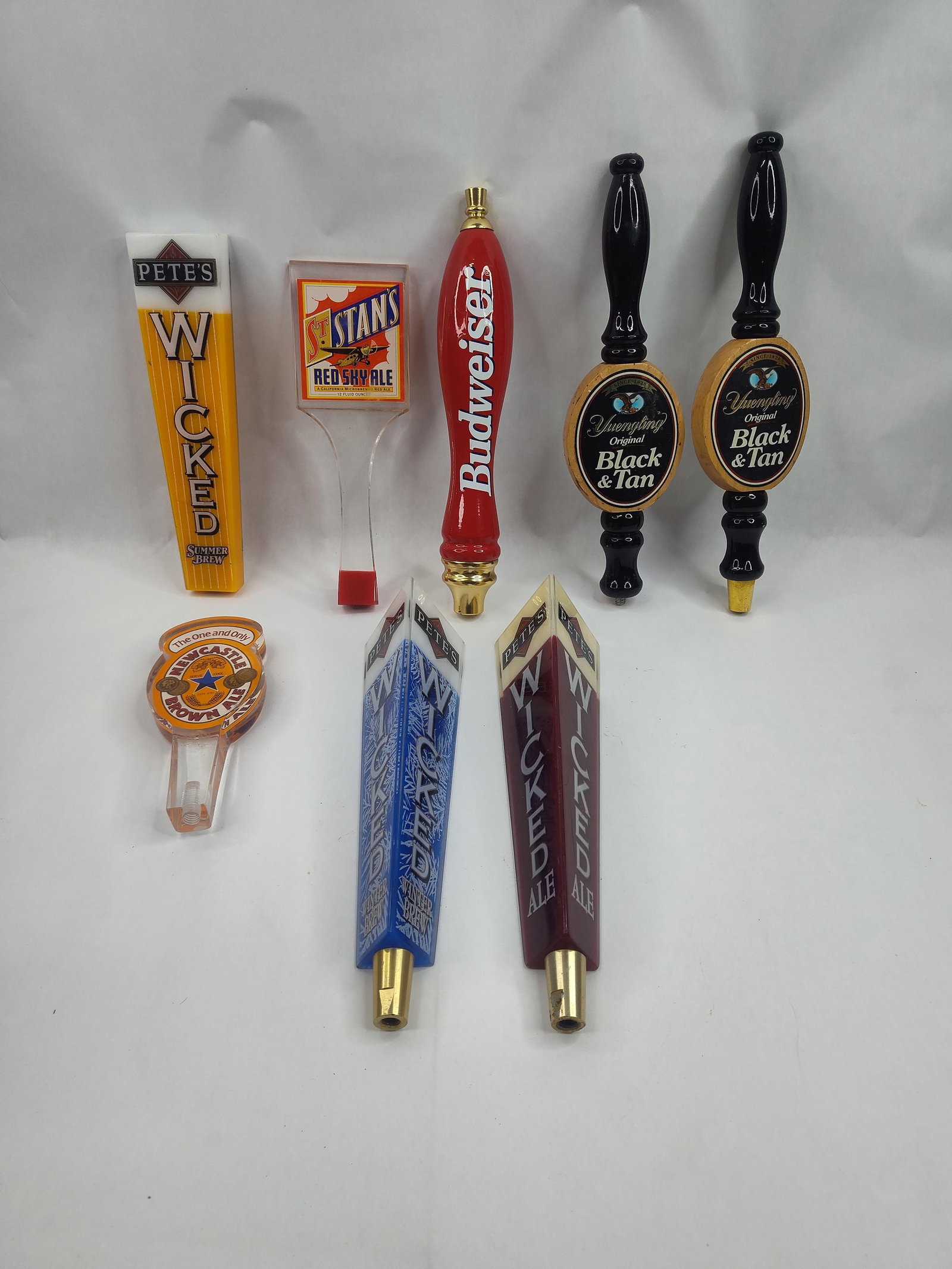 Collection of Beer Tap Handles: An assortment of beer tap handles constructed from acrylic, wood, and metal, featuring branding for various domestic and imported breweries. The group includes several triangular acrylic handles for
