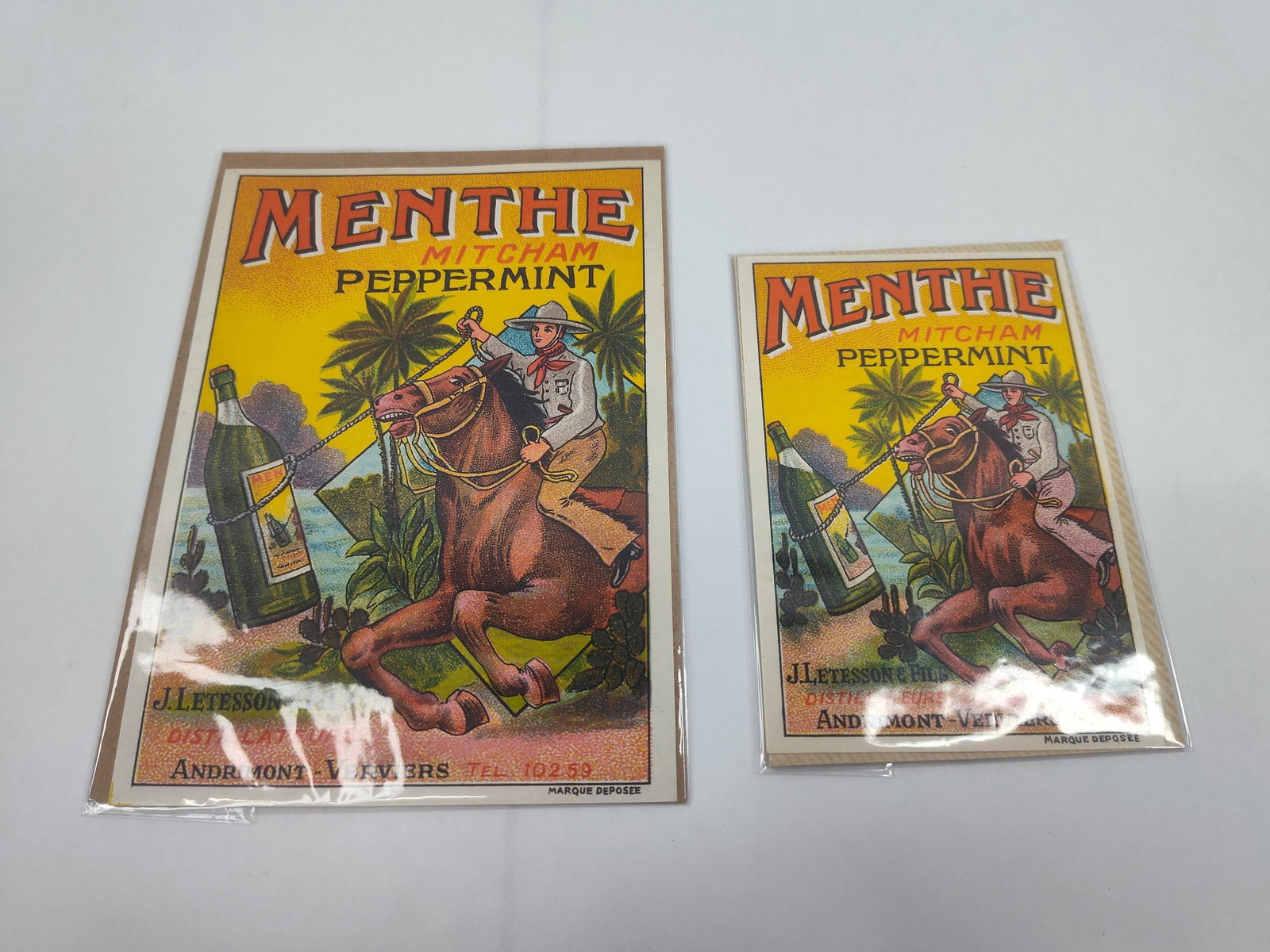 Pair Menthe Mitcham Peppermint Lithos: This lot consists of two lithographic advertising cards for Menthe Mitcham Peppermint, featuring a stylized illustration of a rider on a galloping horse using a lasso to pull a large green bottle of