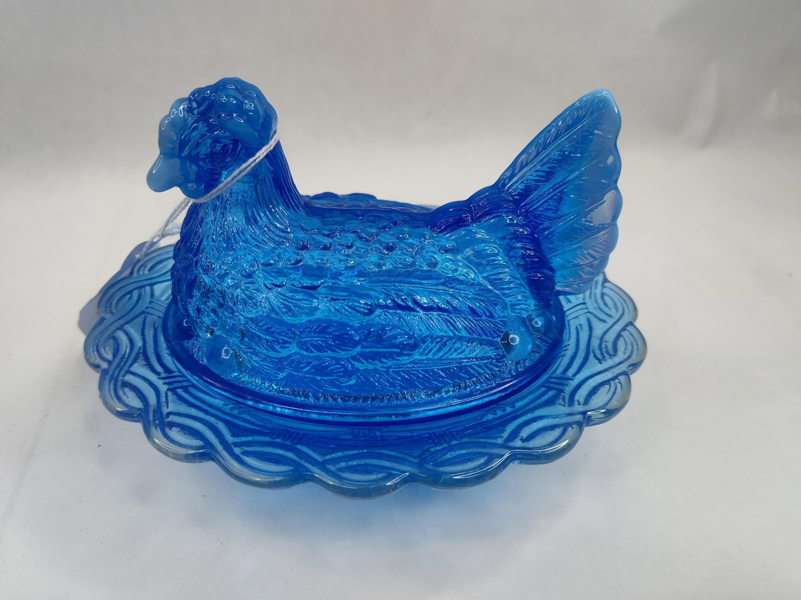 Blue Glass Hen on Nest Covered Dish: A translucent cobalt blue pressed glass covered candy dish in the form of a nesting hen. The lid is molded as a stylized hen with deep feather textures and a wide, serrated tail. The tail feathers and