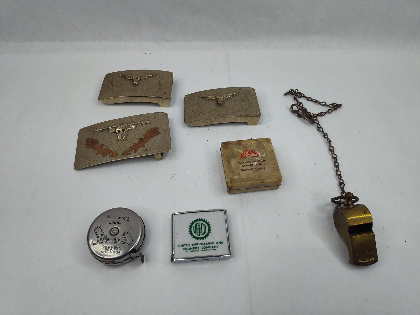 Belt Buckles, Tape Measures &: An assortment of mid-20th-century metalware and industrial advertising ephemera. The collection includes three western-style belt buckles. Two smaller rectangular buckles are constructed of alpaca sil