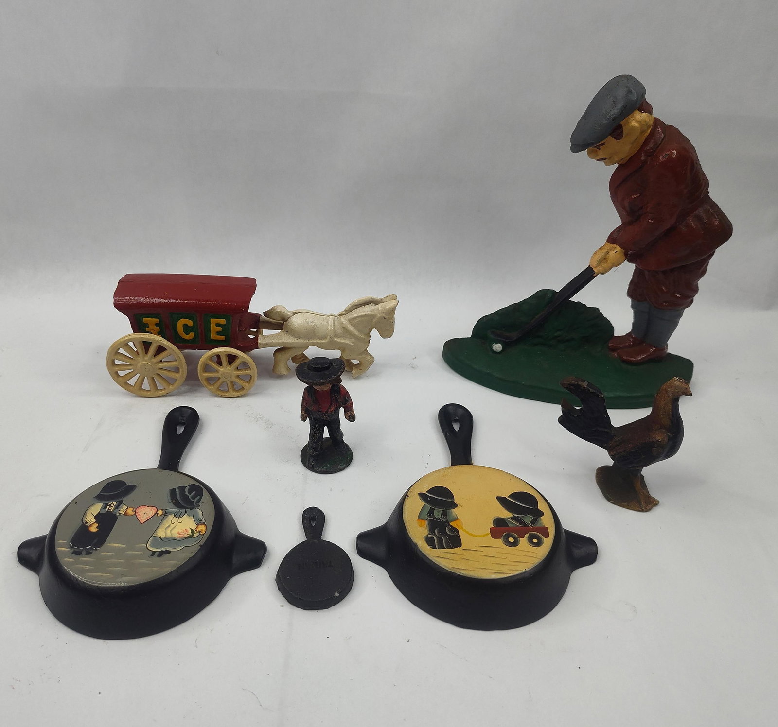 Set Painted Cast Iron Wagon & Skillet: A collection of painted cast iron decorative objects and miniatures. The group includes a golfer figure in a red suit and grey flat cap positioned on a green base, a horse-drawn ice wagon with a red
