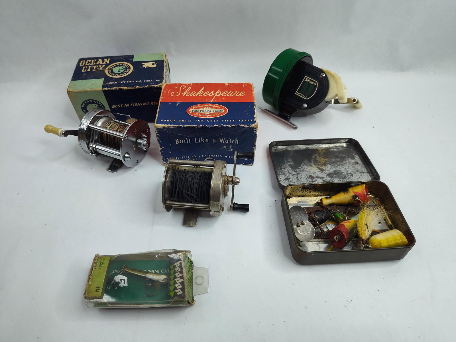 Fishing Reels & Lures, Shakespeare: A collection of mid-century fishing equipment comprising several reels, a variety of lures, and two specialized tins. The group includes an American-made Ocean City 1800 baitcasting reel featuring a