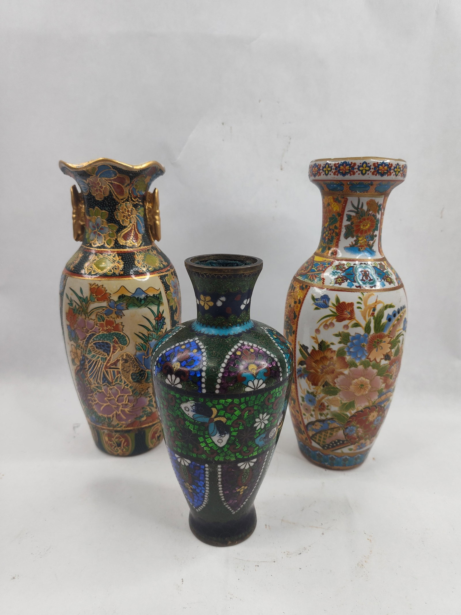Set 3 Asian Vases, Cloisonne & Porc: A trio of decorative vases composed of various materials and techniques. The collection includes a porcelain Satsuma style vase featuring a lobed rim and two gilded handles. The body is decorated with
