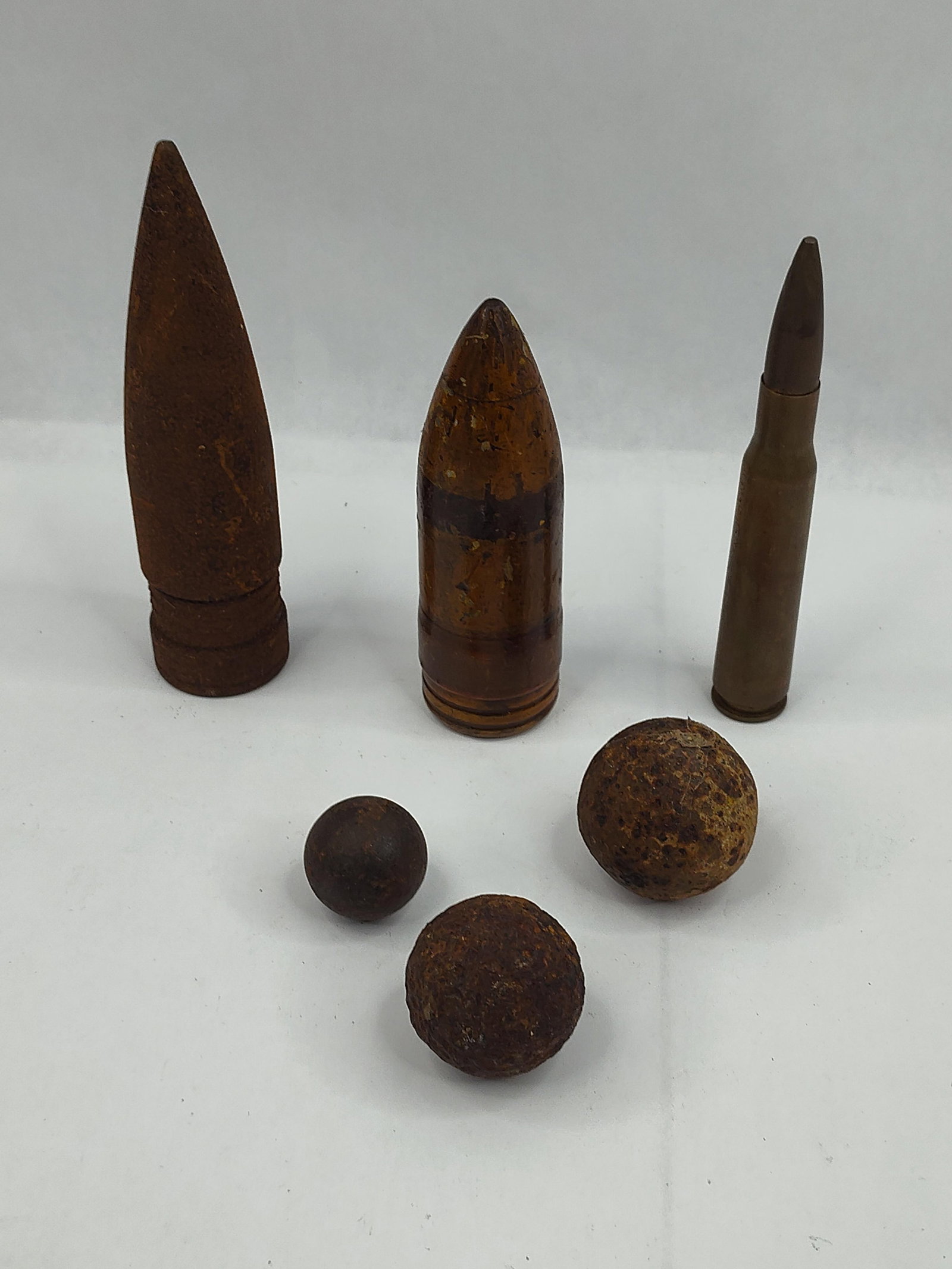 Set of Historical Projectiles & Shells: An assortment of historical militaria comprising six individual pieces of varied munitions. The group includes three spherical solid-shot projectiles of differing sizes, likely iron or lead based on t