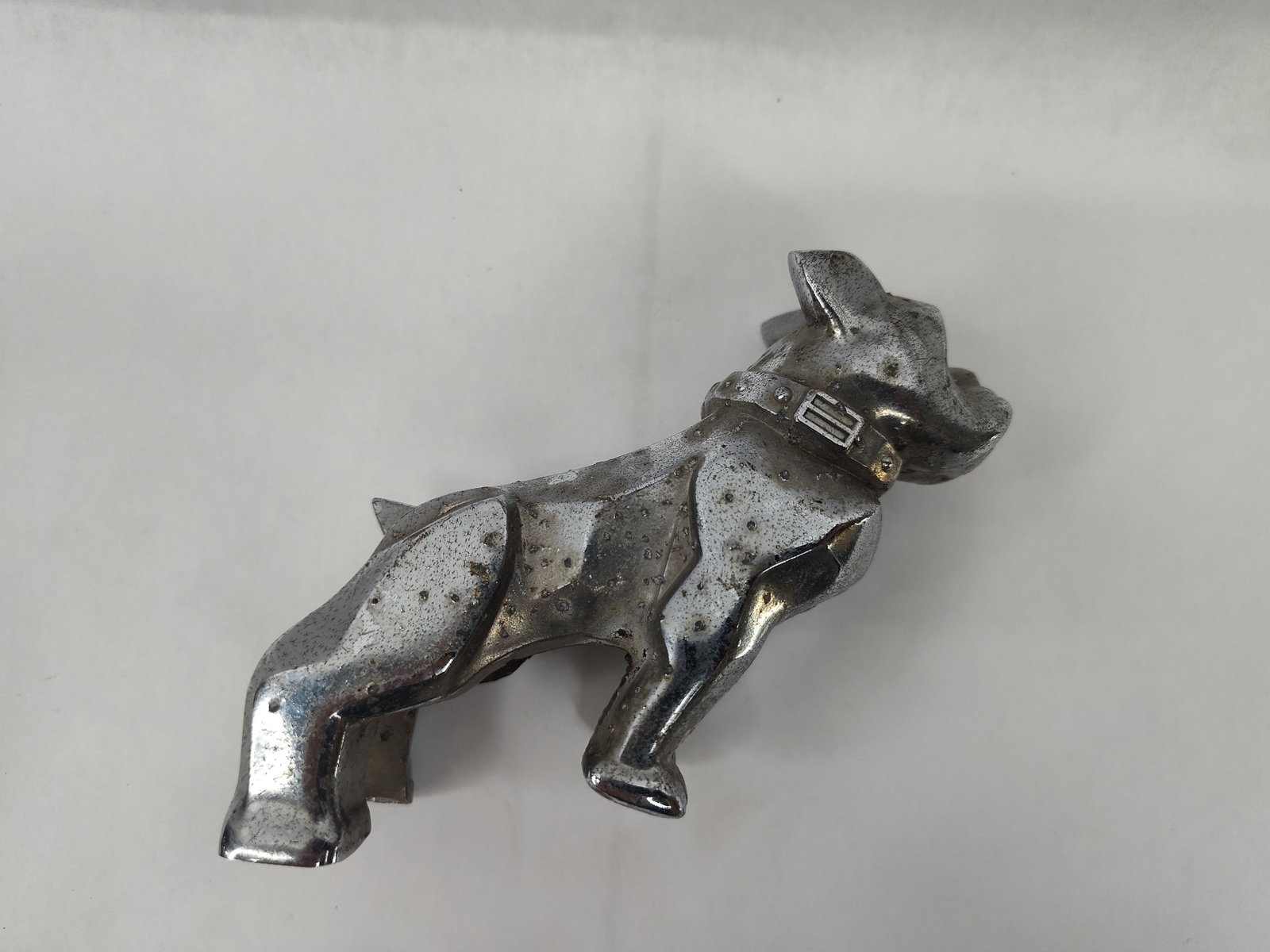 Mack Truck Chrome Bulldog Ornament: A Mack Trucks hood ornament in the form of a standing bulldog mascot. The piece is constructed of chrome-plated metal and features a forward-leaning, stylized muscular pose. The bulldog is modeled wea