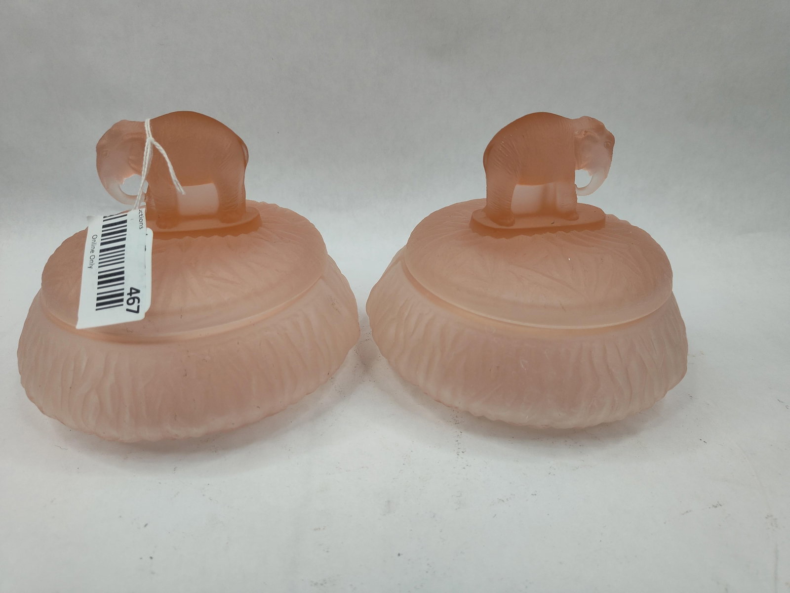 Pair Pink Glass Jars w/ Elephant: A pair of vanity powder jars in translucent pink glass with a matte, acid-etched frosted finish. Each jar is composed of a circular base with a matching lid. The lids feature a molded finial in the