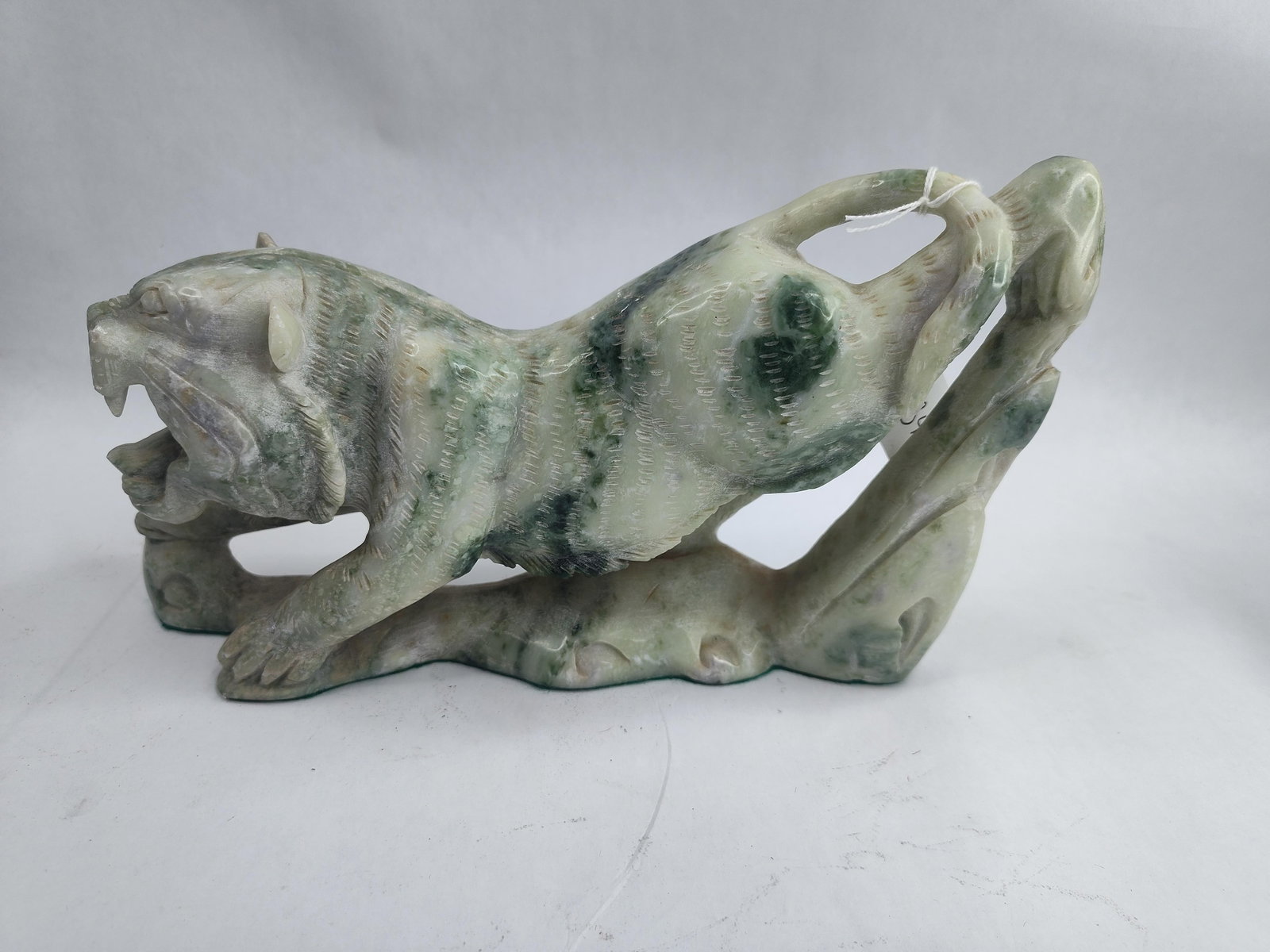 Stone Tiger Sculpture: A hand-carved stone sculpture depicting a tiger in a pouncing stance with an open mouth and bared teeth. The piece is fashioned from a single block of variegated stone, featuring tones of pale gray an
