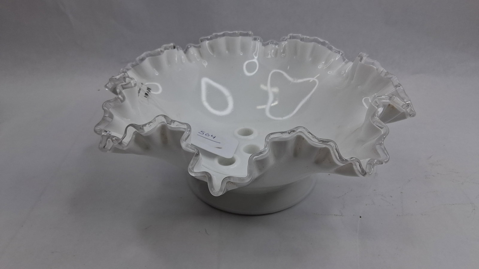 Fenton Milk Glass Flower Frog Bowl: A white milk glass bowl featuring a deep ruffled rim with an applied clear crystal edge, identifying the Fenton Silver Crest pattern. The vessel is designed with a footed base and a central interior w