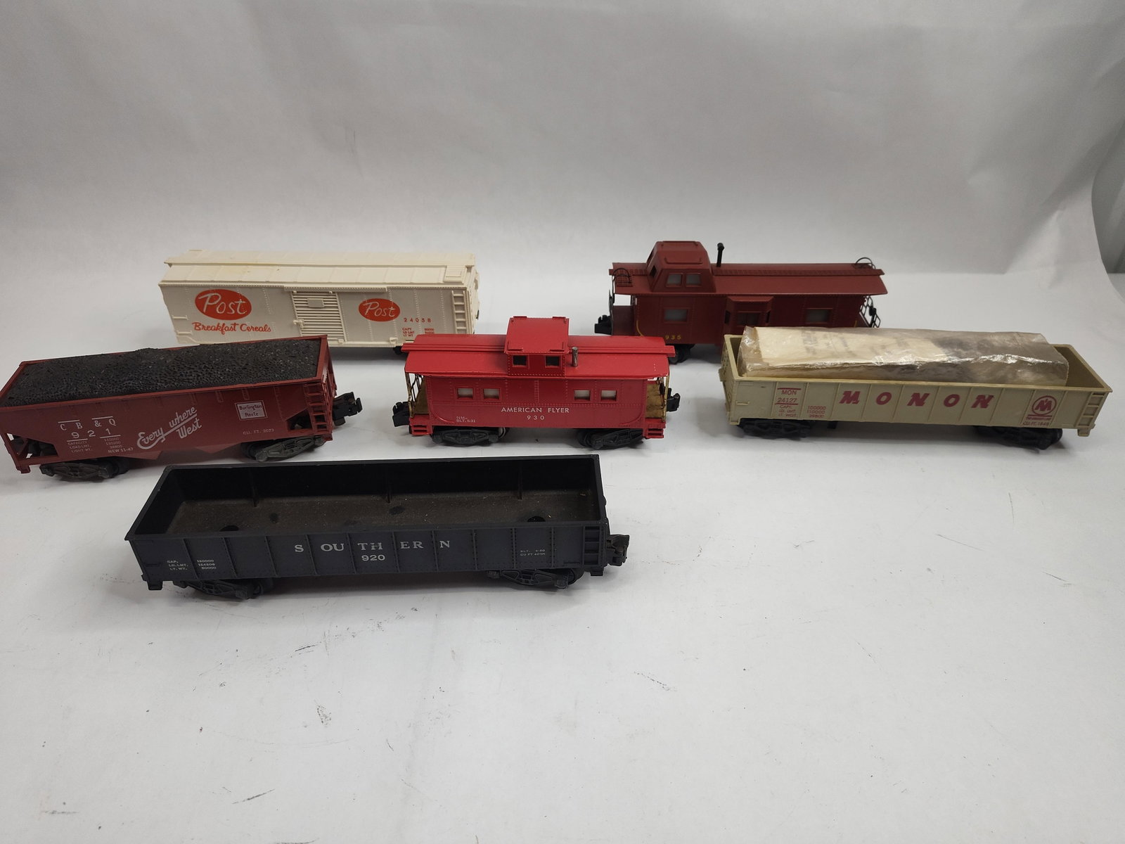 American Flyer S-Gauge Rolling Stock: S-gauge model railroad freight cars and cabooses, featuring plastic bodies, die-cast metal trucks, and metal wheels. The set includes two cabooses, one hopper, one boxcar, and two gondolas. The collec