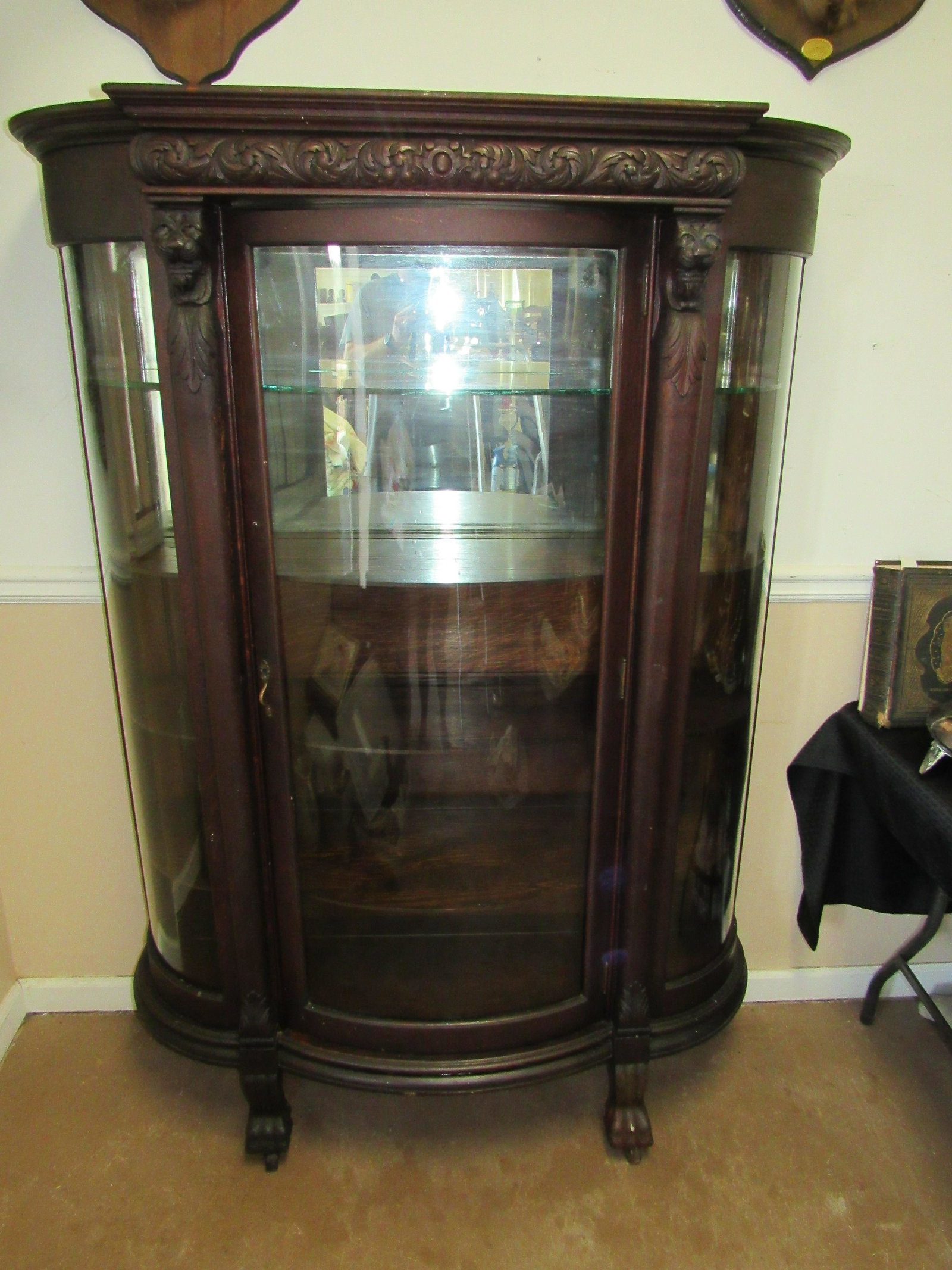 Antique Victorian Bowed Front China Cabinet: Antique Victorian Bowed Front China Cabinet. Constructed of oak with lionhead carvings. Good condition. Comes with 3 original wooden shelves and 1 replacement glass shelf. Door does not close correctl