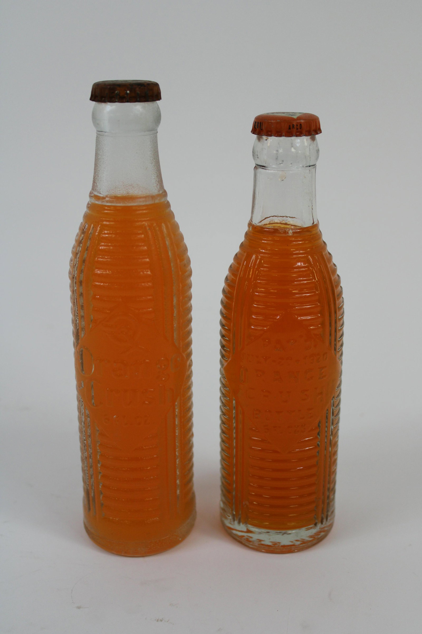 Lot of 2 1920's Orange Crush Bottles with Original Caps: Lot of 2 1920's Orange Crush Bottles With Original Caps and Contents. Overall excellent condition. Contains 1 Bottle from South Boston, VA. Measures 8.25", and 1 bottle from Des Moines, IA. Measures 7