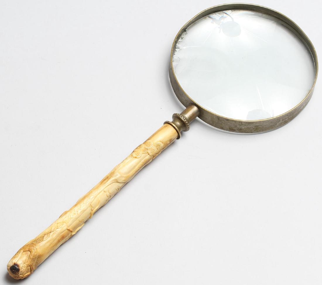 Chinese Carved Bone-Handled Magnifying Glass: The long handle depicting a beauty and a dragon under a tree, some details highlighted with black paint. Handle: 6.75" L; glass: 4.5" diameter; overall: 12.25" L. Some rubbing and tiny burn mark to ha