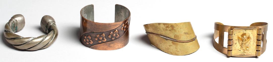 4 Woman's Costume Jewelry Cuff Bracelets: Comprising three thin metal cuffs with abstract, floral and gryphon designs, and a heavy African white metal Manilla money bracelet. Largest 2.75" diameter.