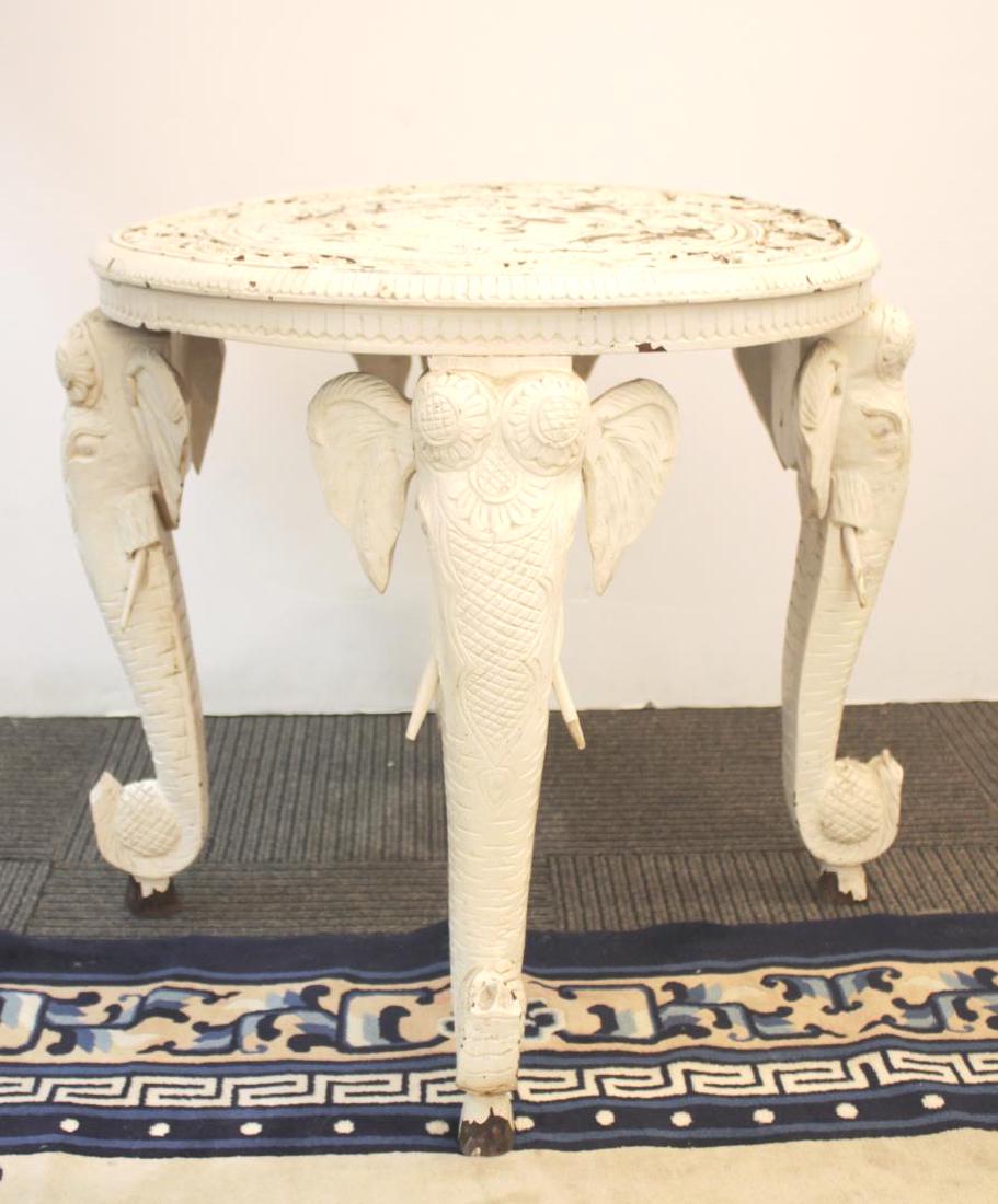 Anglo-Indian Elephant Head Table, Carved & Painted: Anglo-Indian carved and white-painted side table with three elephant head-form supports, each holding a perfume bottle in the curves of their trunks, the top carved with leaves and flowers. 24" H X 23