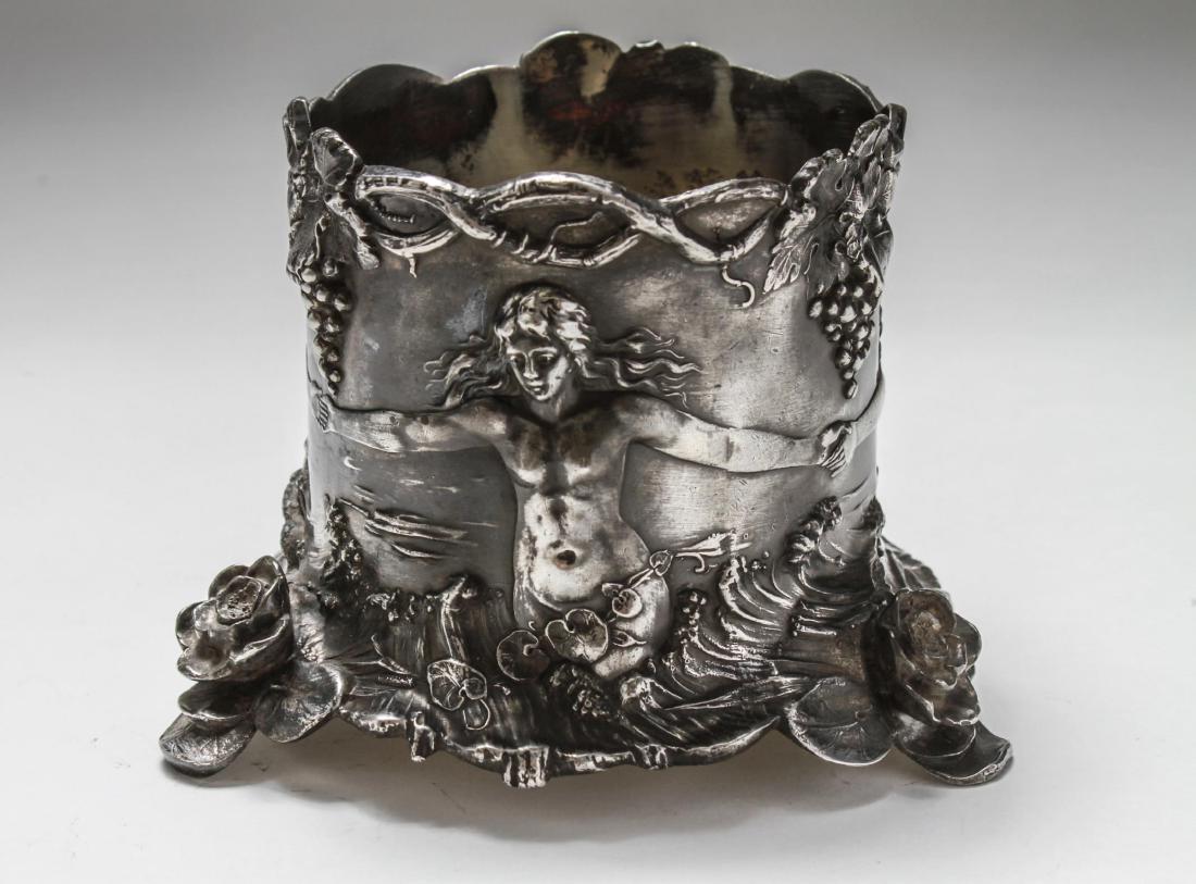 WMF Art Nouveau Silver Plate Wine Bottle Coaster: WMF Art Nouveau silver-plate wine coaster / Champagne bottle holder, the sides with a high-relief embossed frieze of nude women dancing amidst grapevines, the tripod feet with applied roses, the under