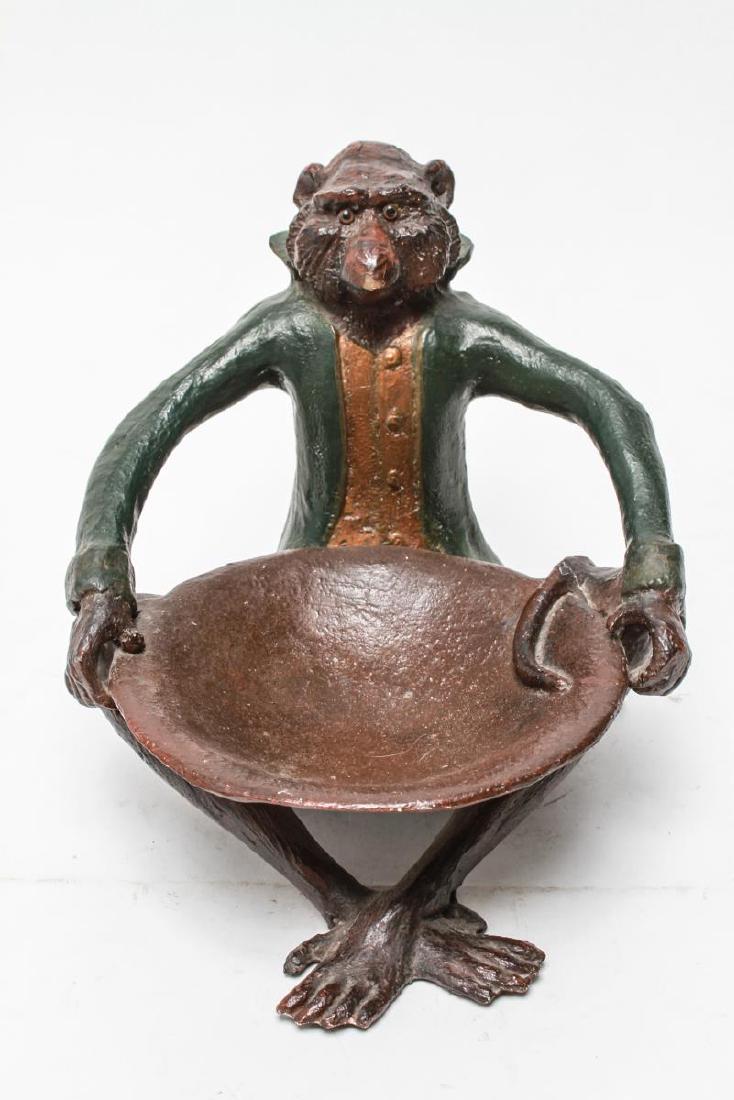 Monkey Butler Table Top Dish, Composite: Monkey butler table top dish, seated monkey wearing long green coat with copper-tone vest holding a dish in his lap, composite. 9.5" H x 9" W x 12.5" D. Paint loss throughout