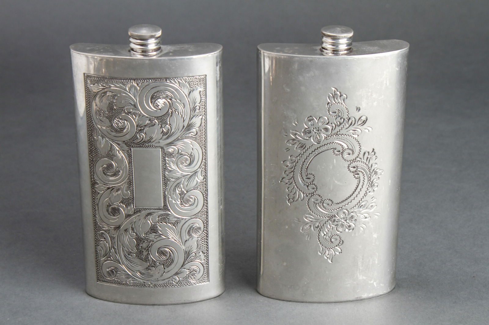 Hoffritz English Pewter Scroll Engraved Flasks, 2: Group of two Hoffritz English pewter scroll-engraved 12 ounce flasks, marked: "Hoffritz / Made in England / English Pewter / 12 Ounce." 7.5" H x 3.75" W x 1.25" D.