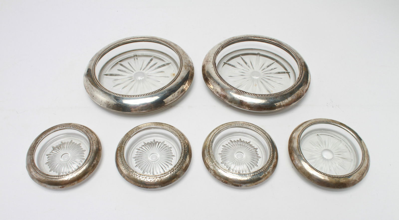 Glass Coasters with Sterling Silver Rims, 6: Group of six glass coasters with sterling silver rims, two Frank M Whiting & Co. wine coasters along with four smaller comprising one Whiting and three Saben, all marked. Largest: 7" diameter. Minor d