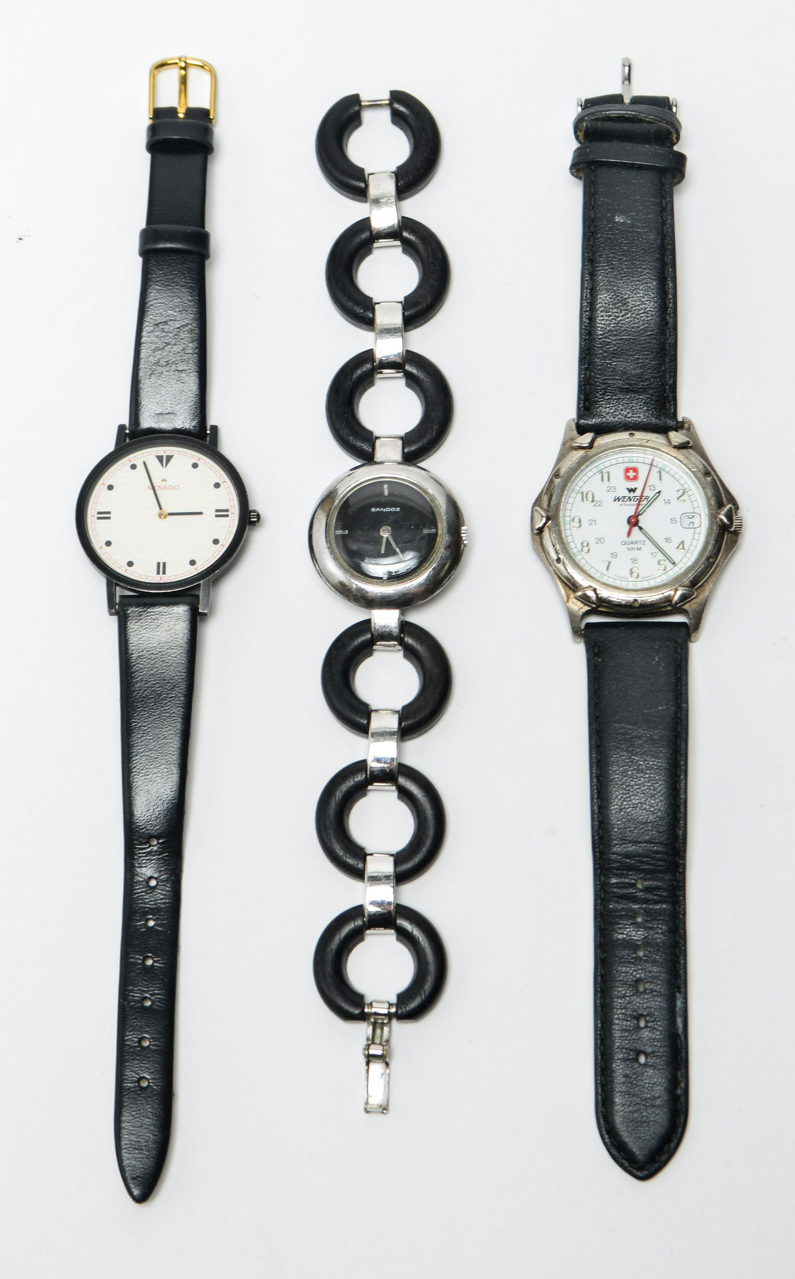 Movado, Sandoz, & Wenger Wristwatches, 3: Three wristwatches, one Movado with cream, red, and black dial, one Sandoz with band featuring circular wood links, and one Wenger, all marked on face. Largest: approx 38mm.