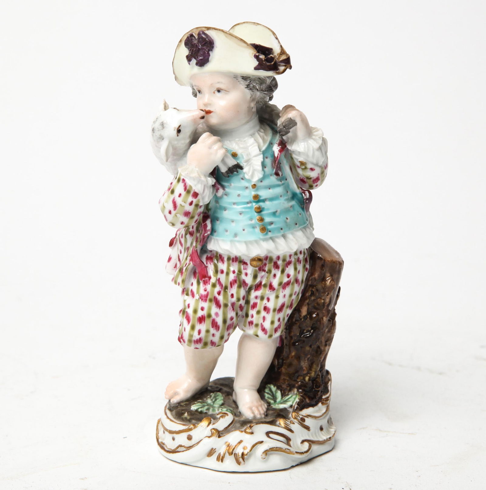 Meissen Porcelain Figure of Shepherd with Lamb: Meissen porcelain figure of a shepherd depicted in 18th century garb carrying a lamb across his shoulders, leaning on a tree stump, on rounded base, bears blue crossed swords mark to underside. 5.5" H