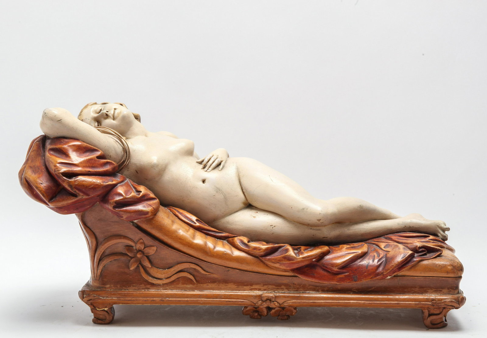 Art Nouveau Manner Figure Of A Reclining Woman: Art Nouveau manner polychrome decorated carved figure of a woman, depicted reclining nude upon a chaise longue. 9.75" H x 20" W x 8" D. Cracks, losses.