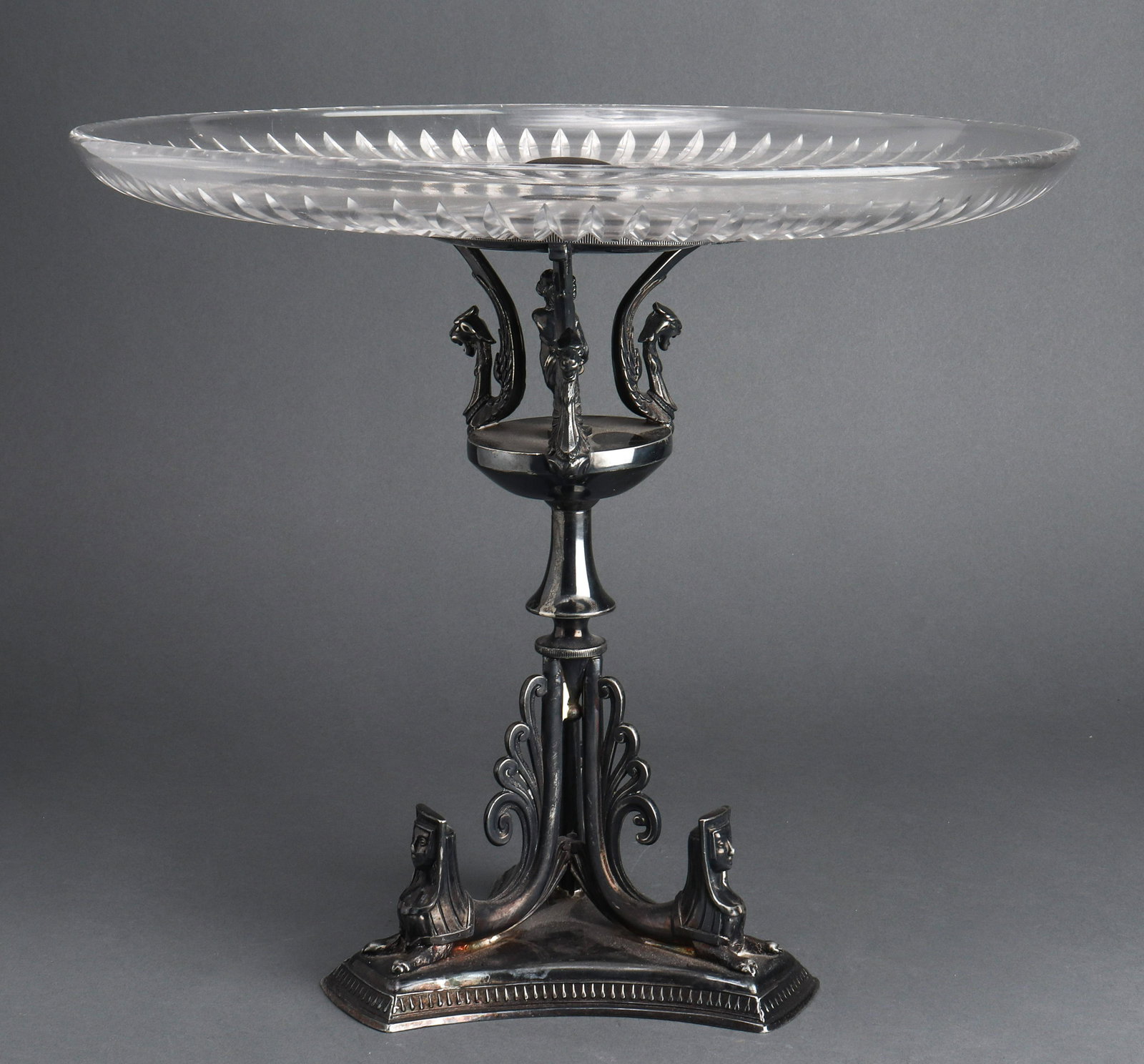 Empire Manner Patinated & Glass Tazza Centerpiece: Empire Manner patinated metal and glass tazza centerpiece, late 20th century, the cut glass dish above the tiered base with stylized figural griffins, maiden, and sphinx supports surmounting a three f